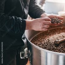 Ein Mann hält Kaffeebohnen in seinen Händen vor einer Kanne mit Kaffeebohnen.