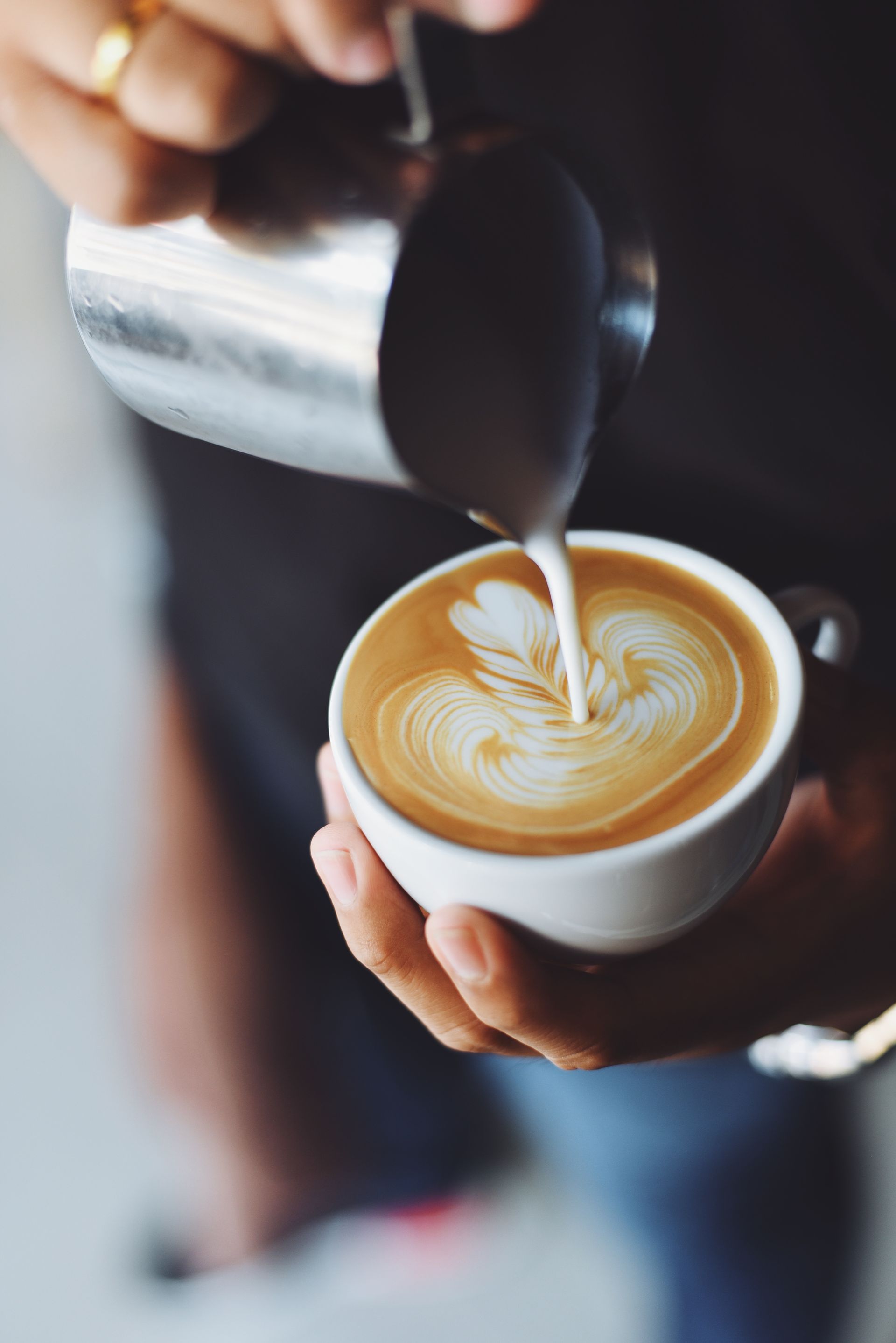 Eine Person giesst Milch in eine Tasse Cappuccino.