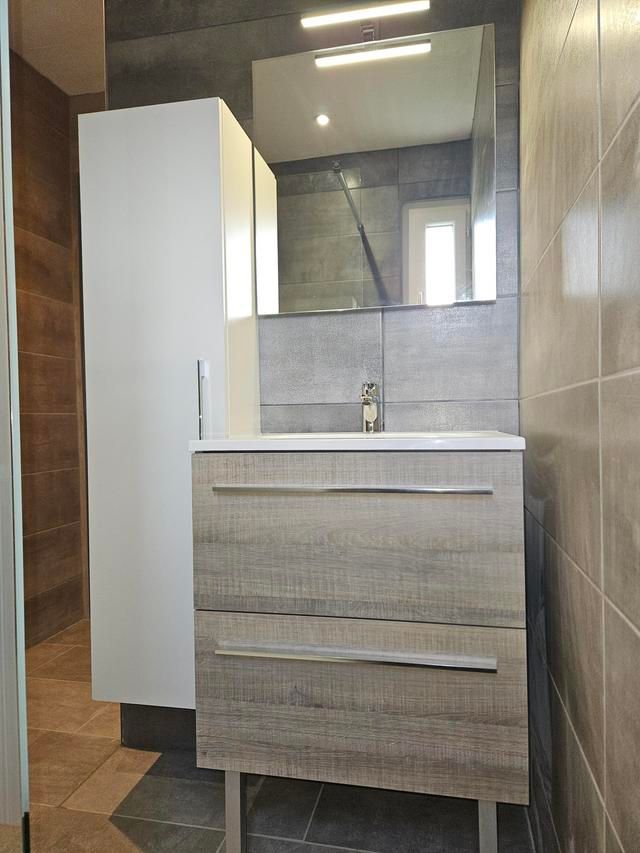 Une salle de bains entièrement carrelée en gris.