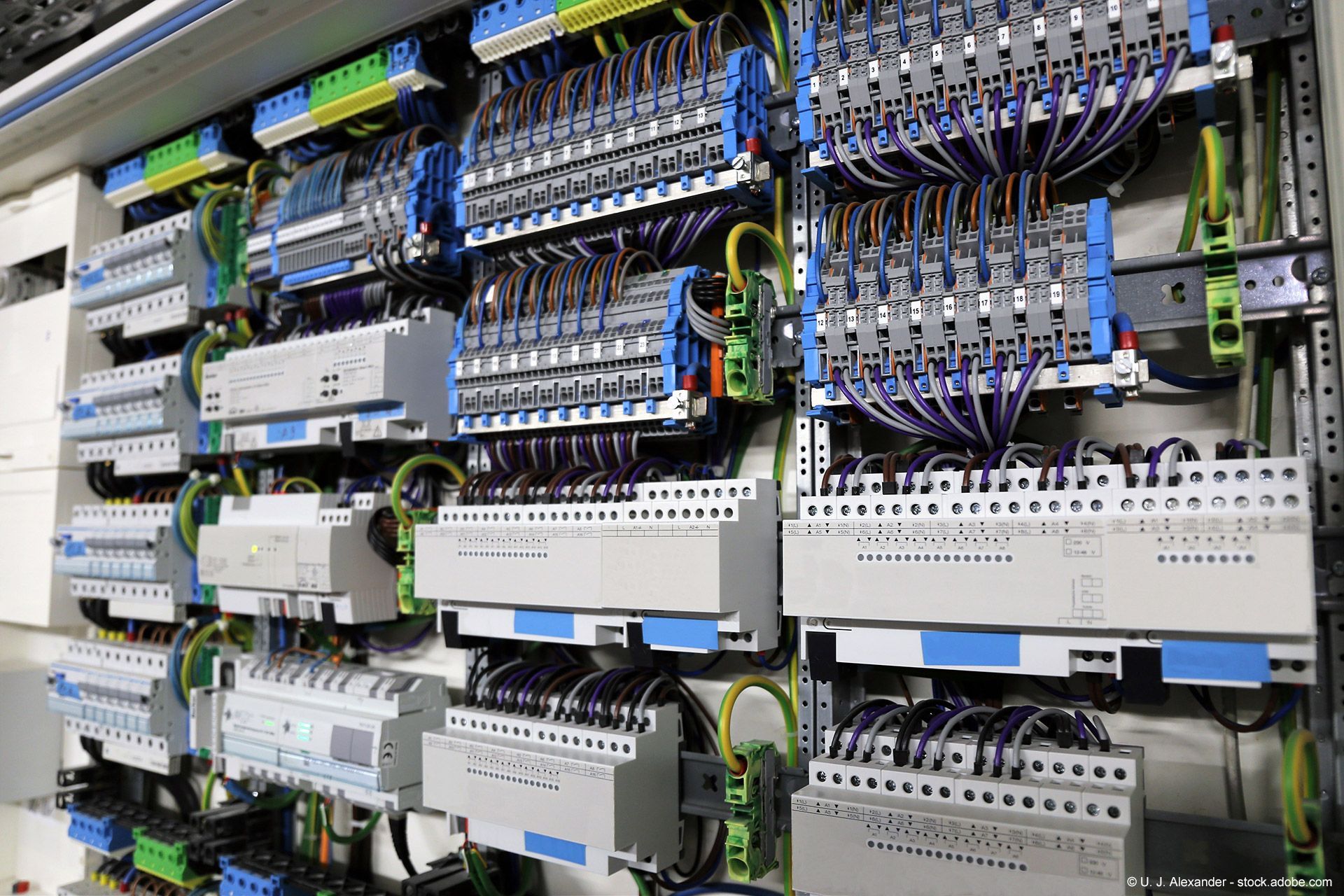 Elektrisches Bedienfeld mit zahlreichen Kabeln, die mit Klemmenblöcken und Leistungsschaltern verbunden sind.