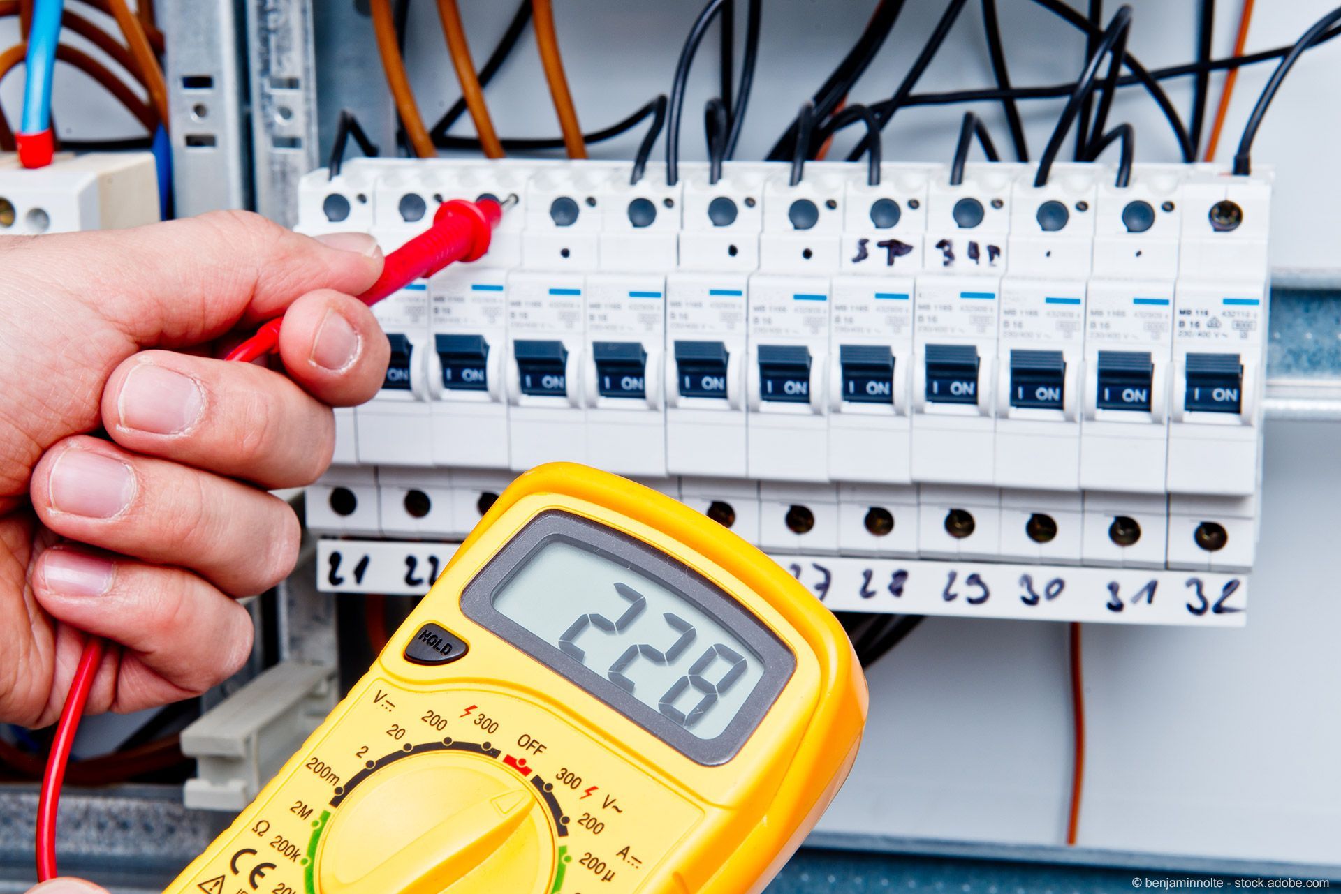 Elektriker testet eine Sicherungstafel mit einem Multimeter, das 228 Volt anzeigt.
