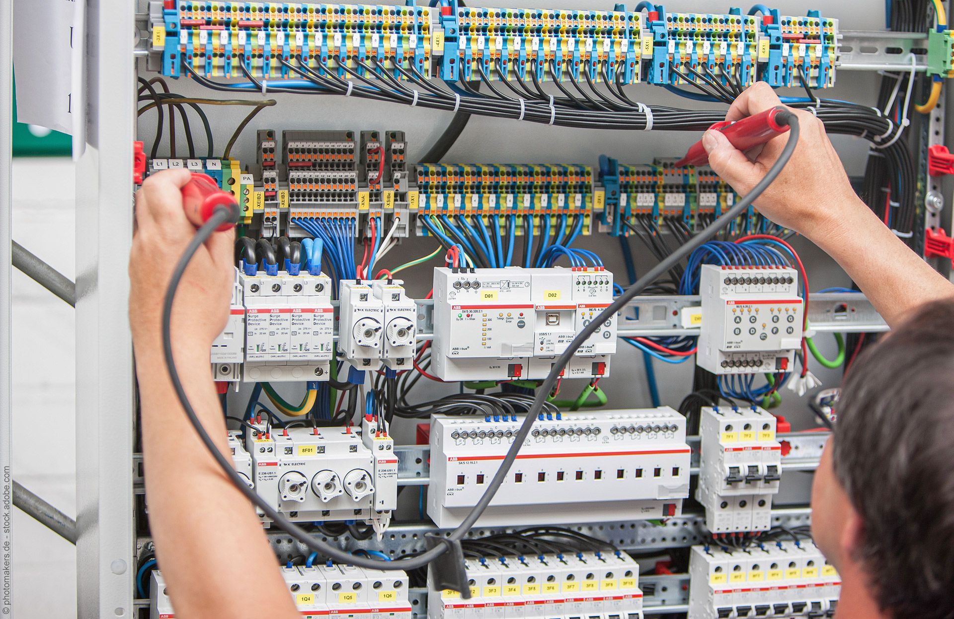Elektriker testet die Verkabelung in einem Bedienfeld mit roten und schwarzen Sonden.