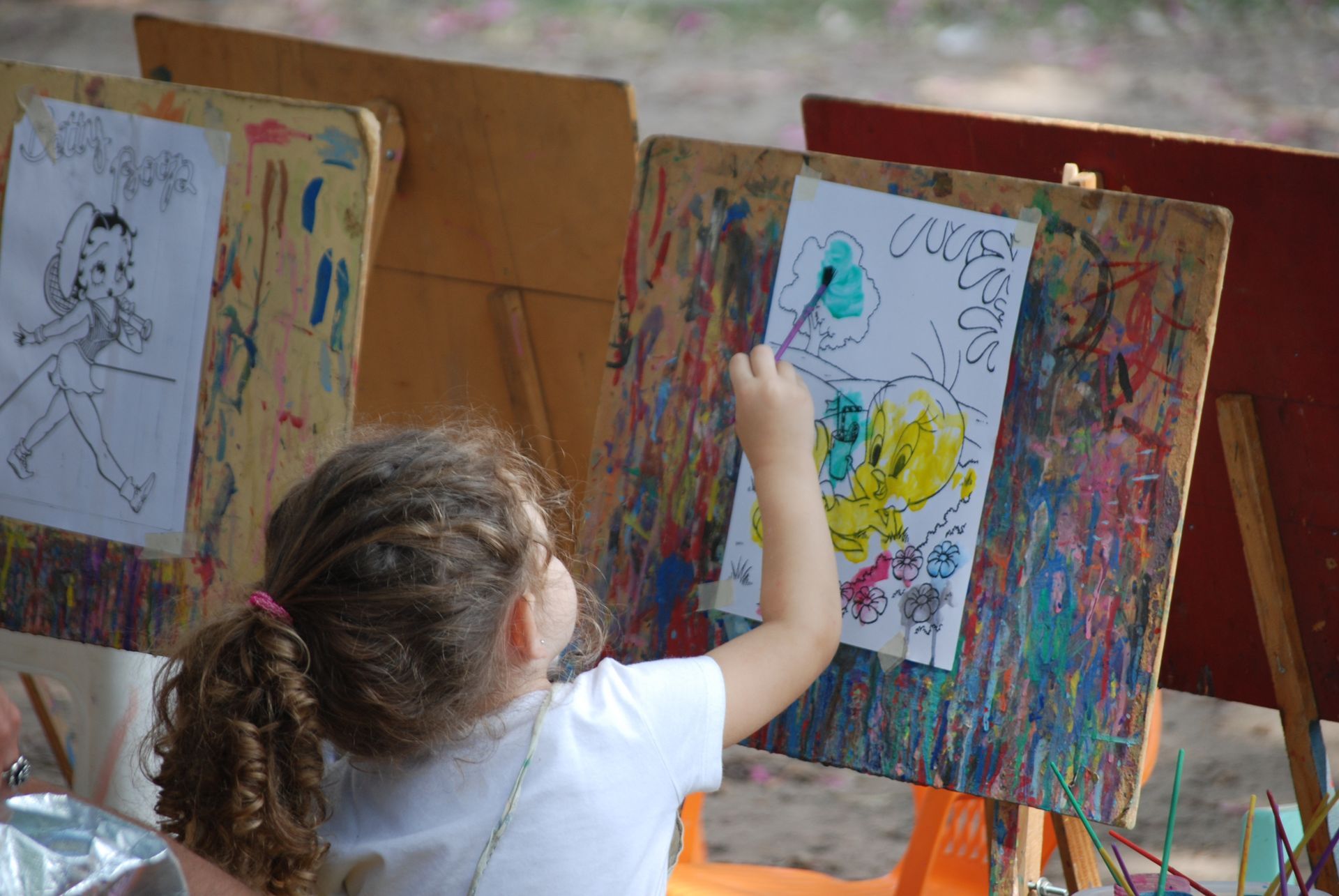 Enfant peignant sur un chevalet lors d'un cours d'art, avec des éclaboussures de peinture colorée et des dessins sur les tableaux