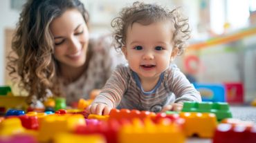 Un adulte et un bébé sourient en jouant avec des blocs de construction colorés sur le sol.