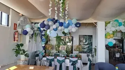 Una sala con mesas y sillas decoradas con globos y flores.