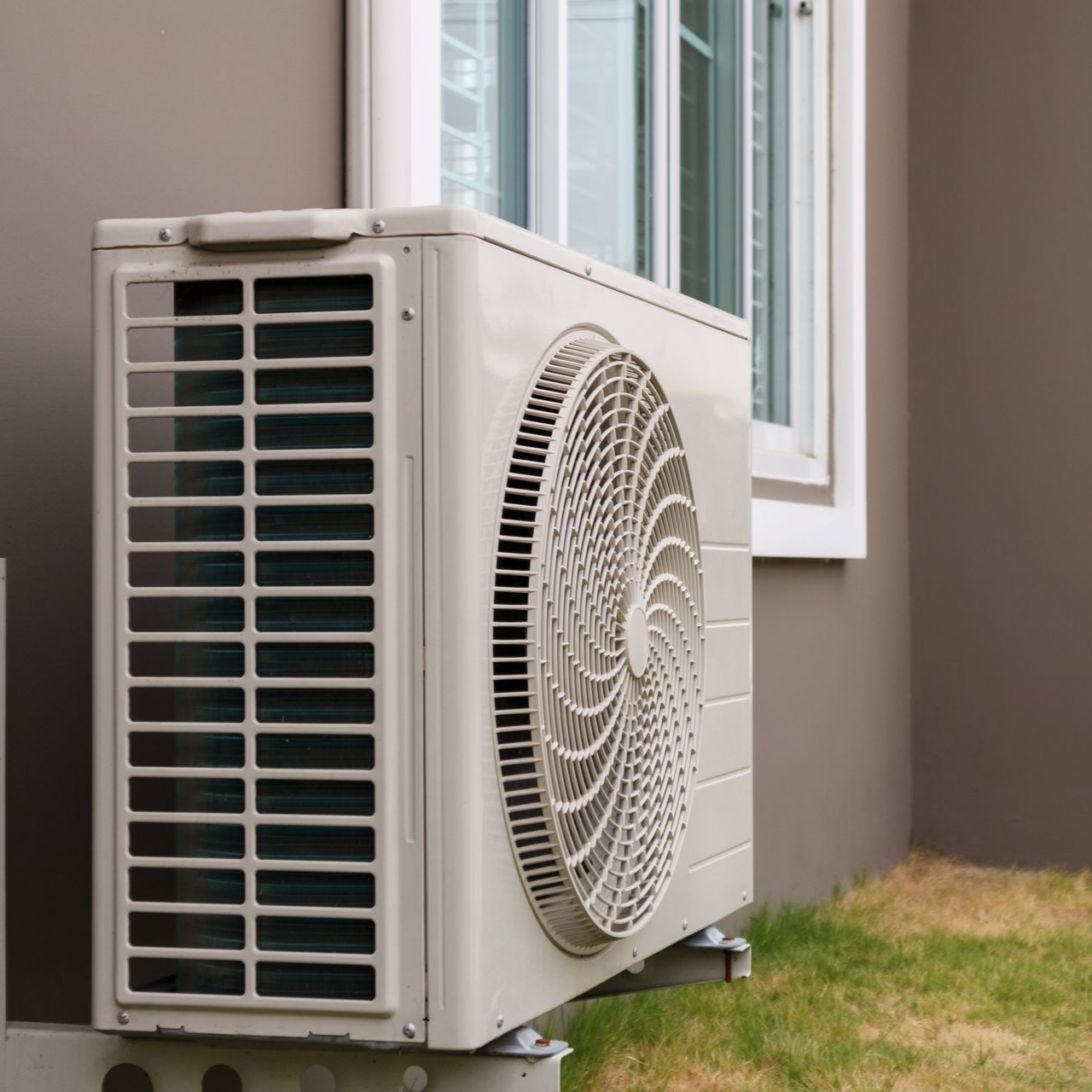 Unité de climatisation extérieure à côté d'une fenêtre de maison.