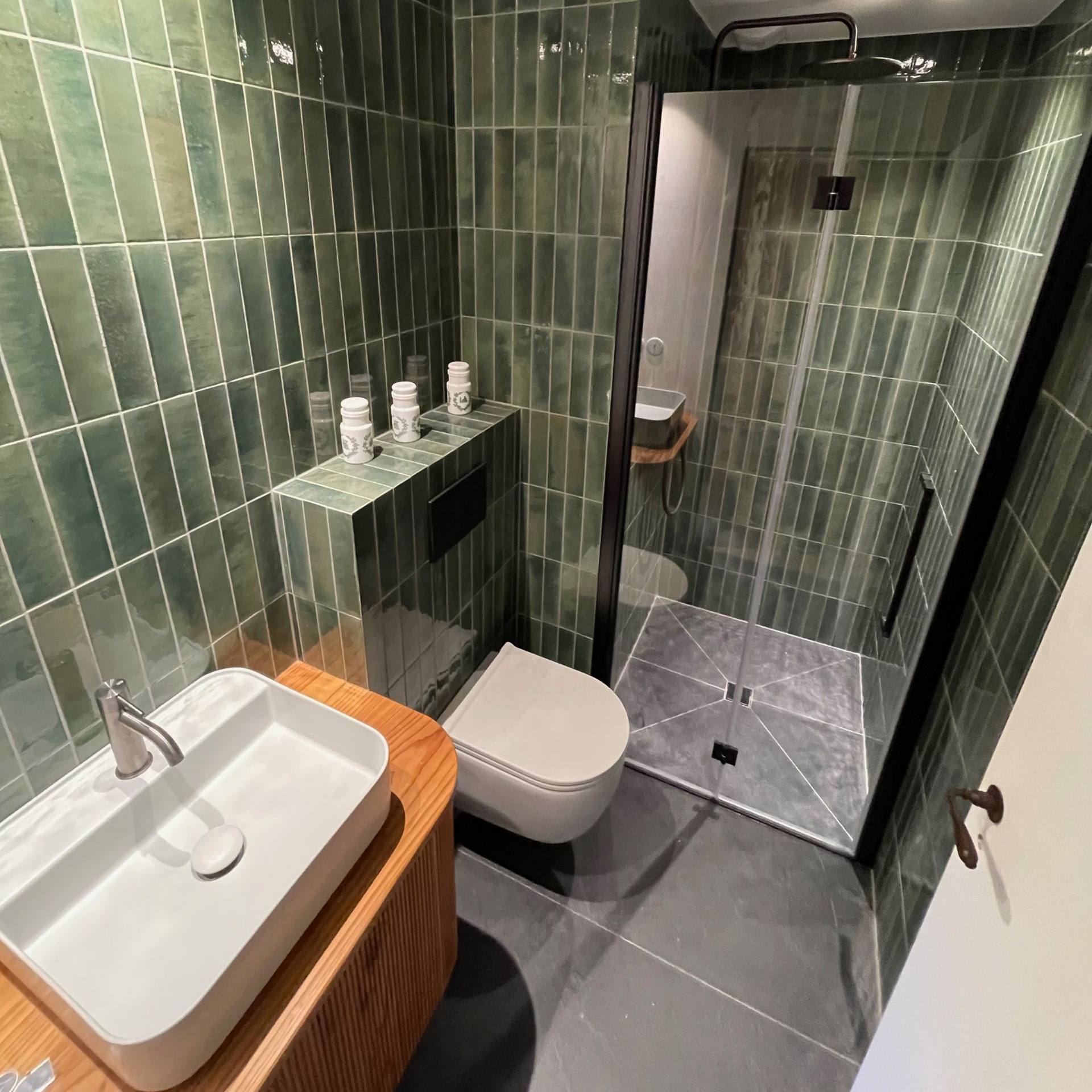 Salle de bains moderne avec douche vitrée, lavabo sur meuble en bois et carrelage mural vert.