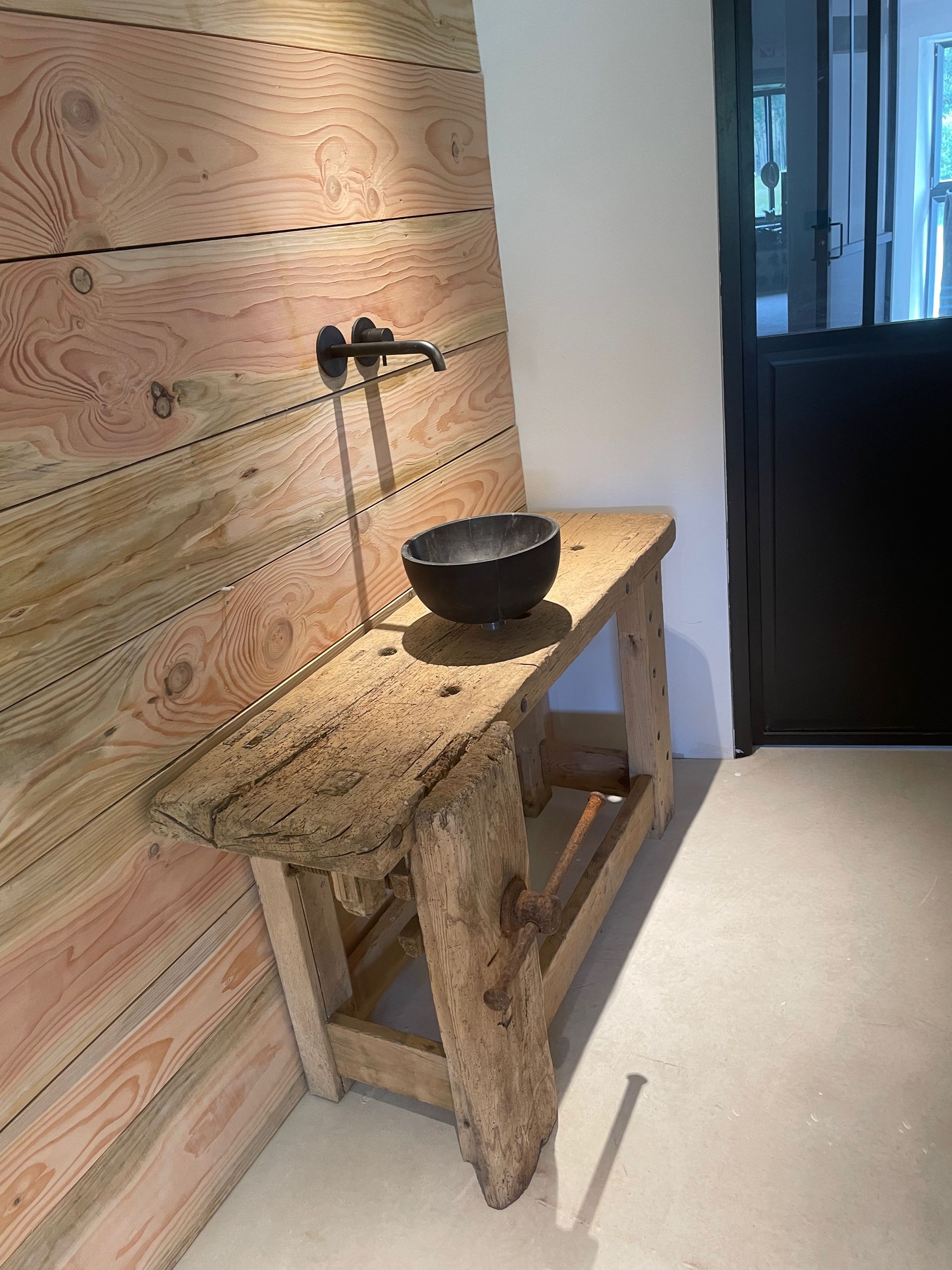 Coin lavabo rustique en bois avec vasque noire et robinet mural.