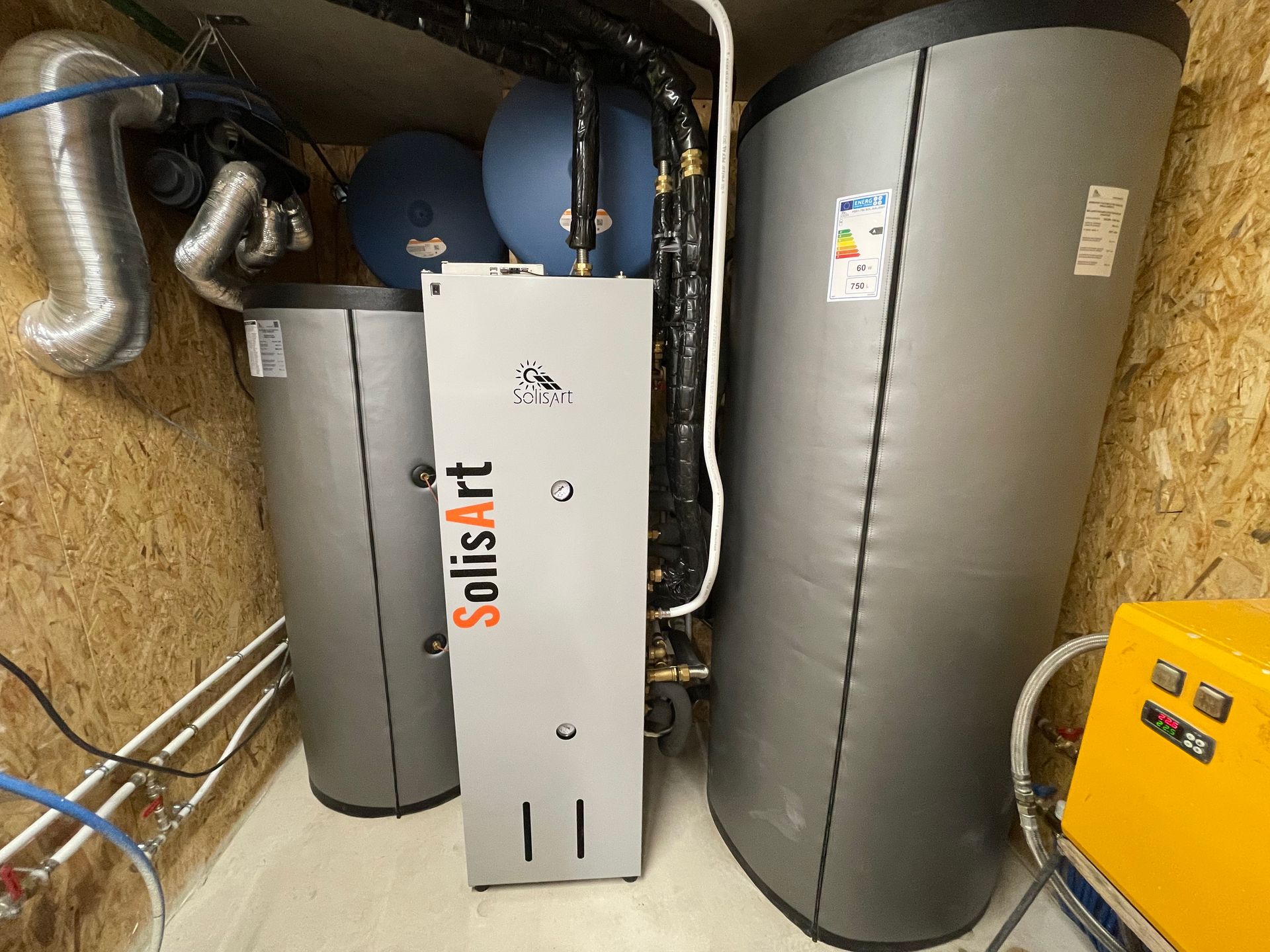 Chaufferie avec réservoirs isolés, tuyauterie et chauffe-eau solaire blanc entre les murs en panneaux OSB.