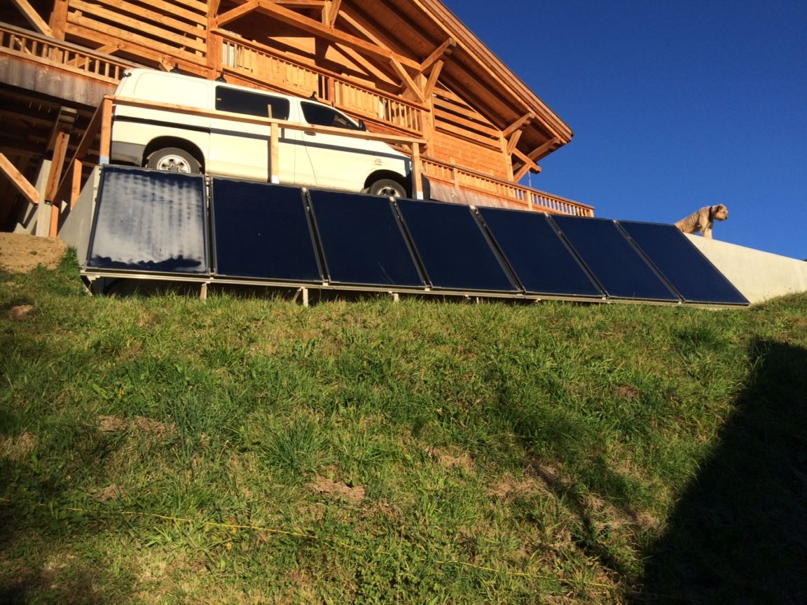 Des panneaux solaires alignés sur une pente herbeuse, à côté d'une camionnette blanche et d'un chalet en bois.
