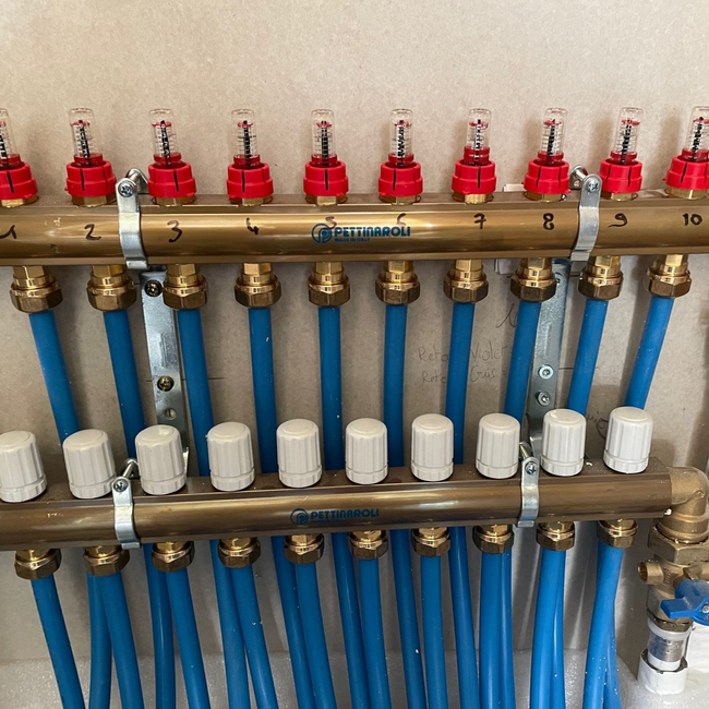 Collecteur de plancher chauffant avec tubes PER bleus et débitmètres de réglage.
