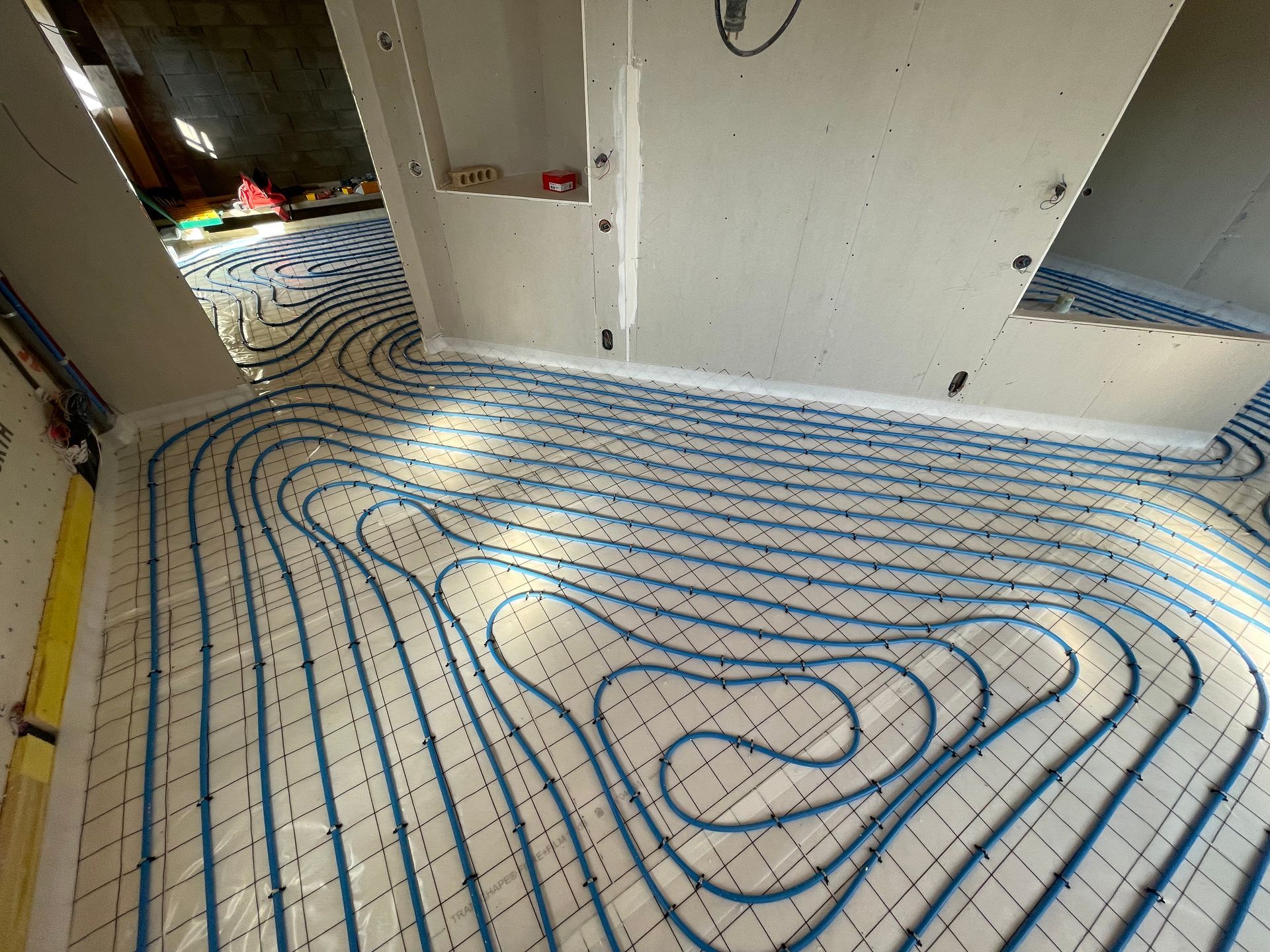 Installation de plancher chauffant avec tubes hydrauliques bleus posés sur une isolation de sol avant coulage de la chape.