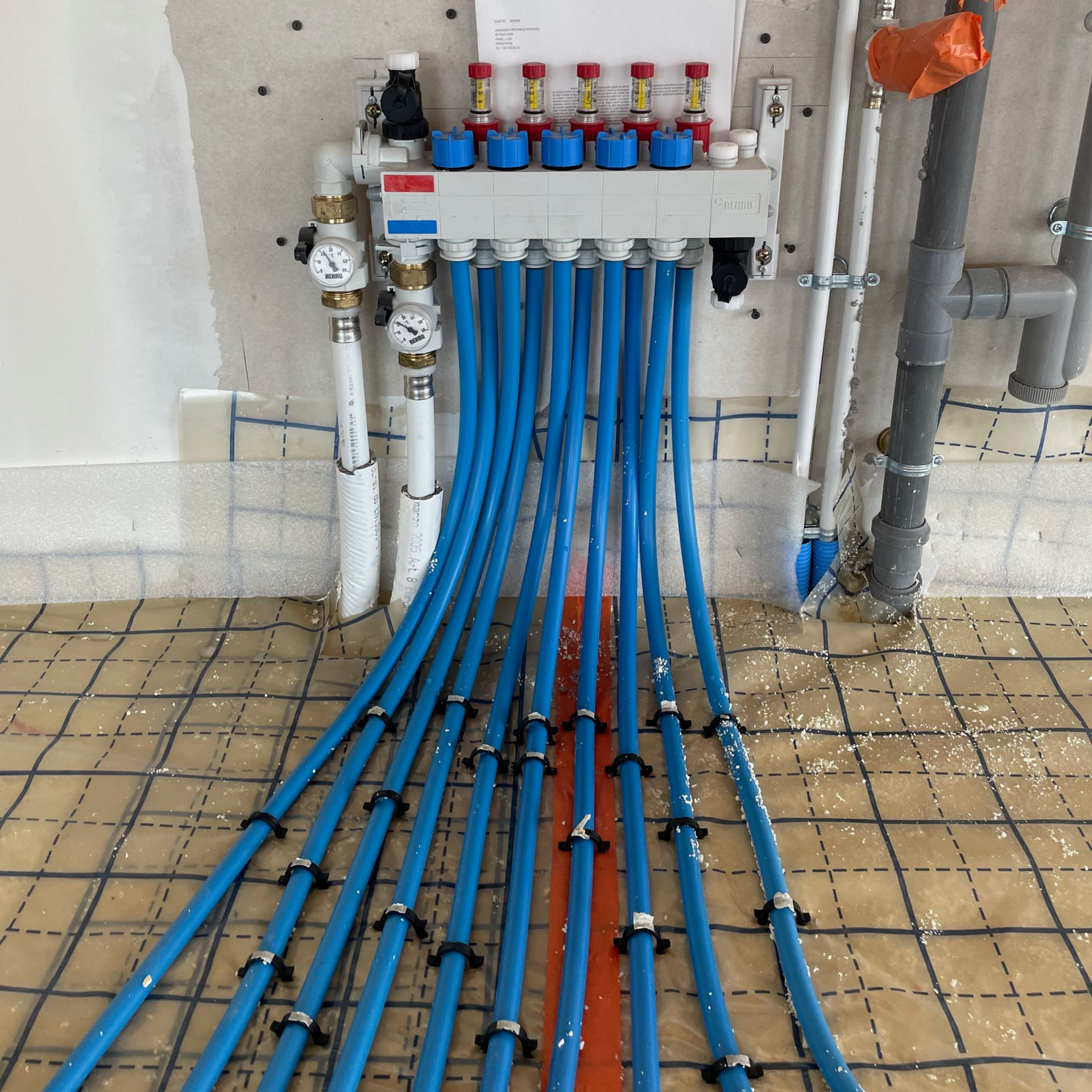 Collecteur de chauffage au sol avec plusieurs circuits hydrauliques raccordés à des tubes bleus dans une maison en construction.