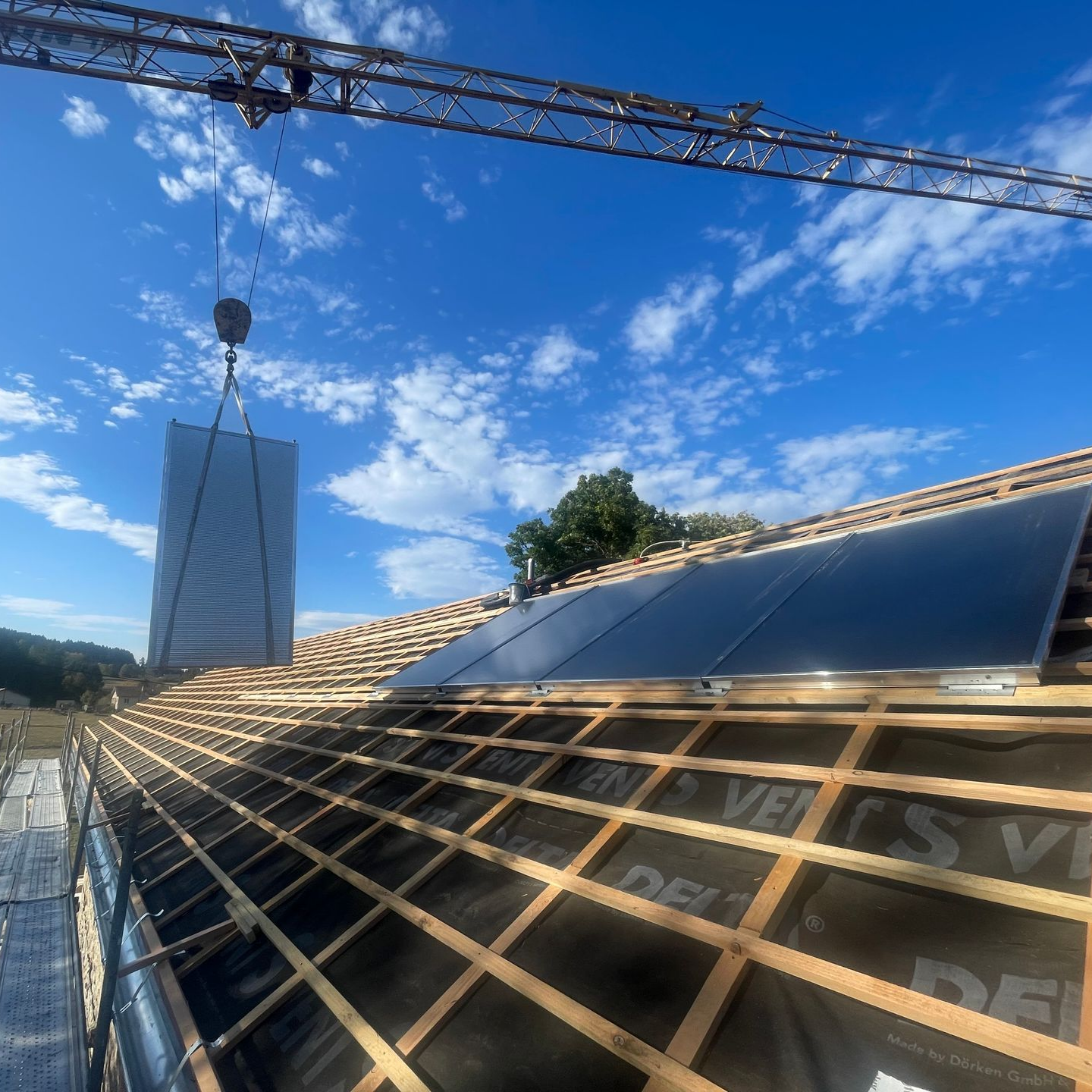 Toiture en construction avec panneaux solaires déplacés par une grue.