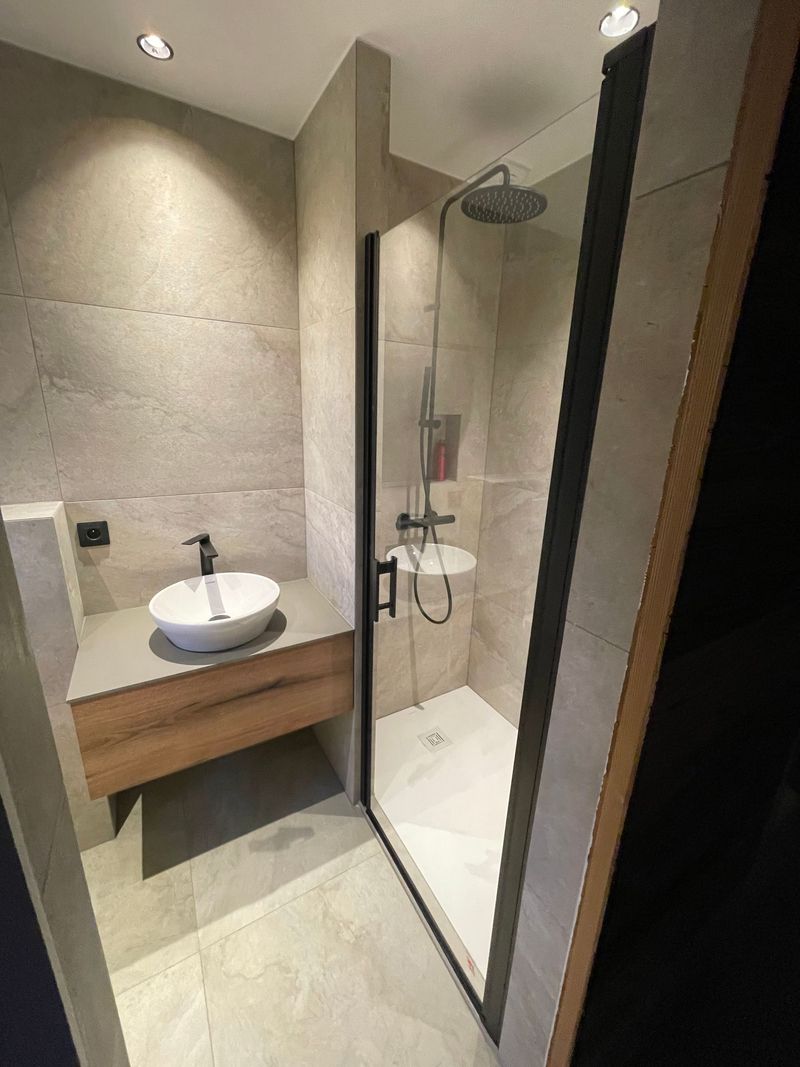 Petite salle de bains moderne avec murs en pierre, vasque blanche ronde avec meuble en bois et douche à l'italienne.