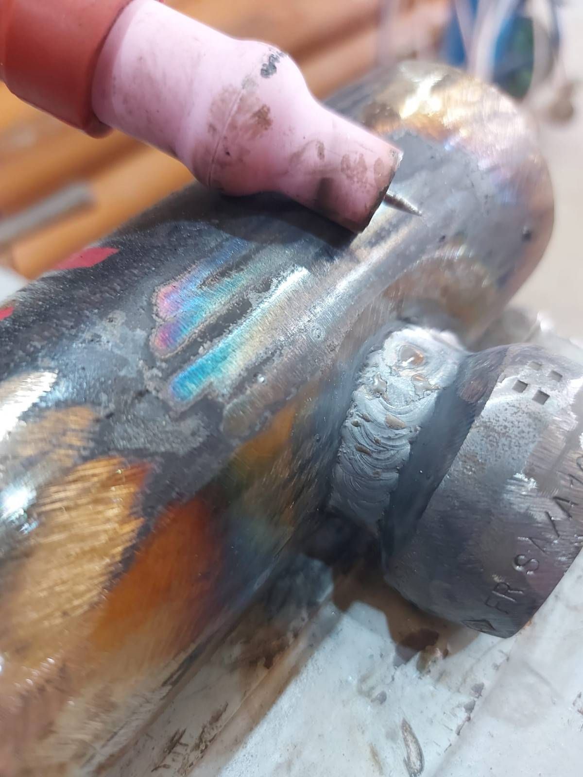 Mano sosteniendo una pieza de tubería metálica desgastada y grasienta, con manchas de óxido y pintura.