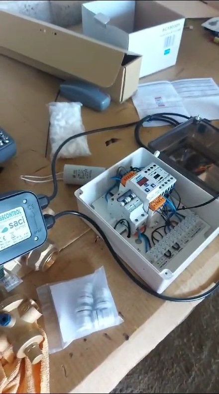 Caja de componentes electrónicos abierta con cableado y módulos sobre una mesa de madera, rodeada de materiales de embalaje.