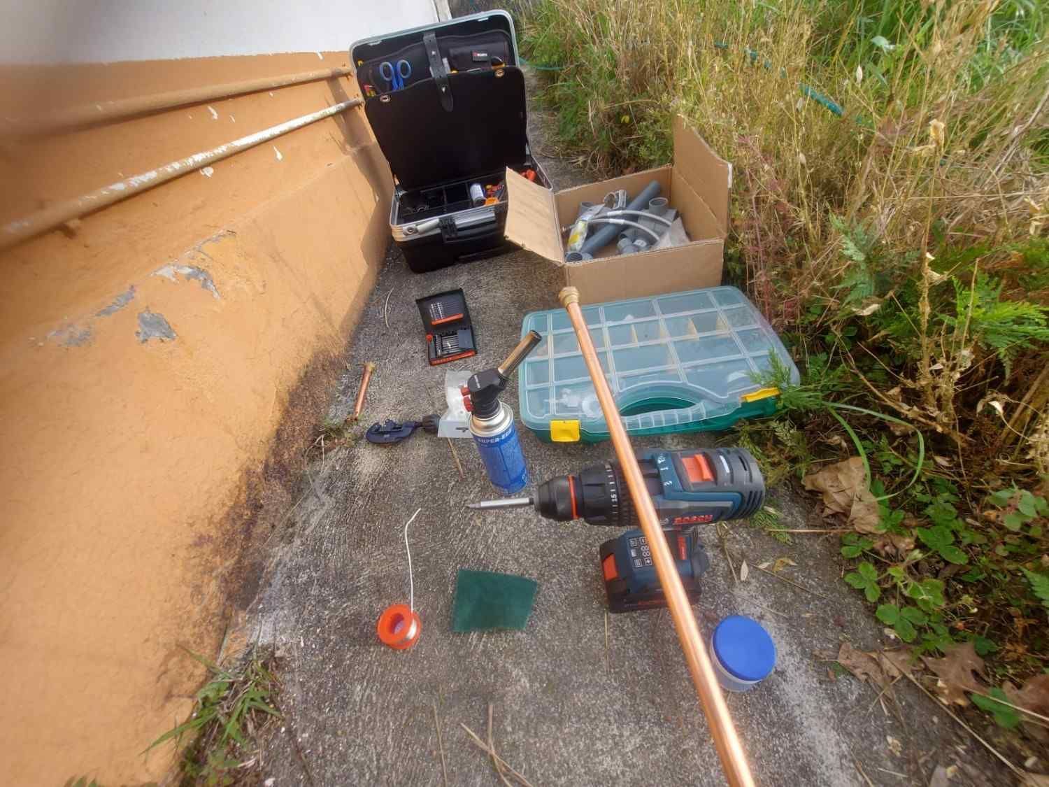 Un kit solar portátil y sus herramientas están extendidos sobre el pavimento junto a un muro y la hierba crecida.