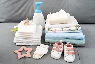 Elementos esenciales para bebés en un sofá gris: pañales, mantas, loción, zapatos, calcetines y juguetes con forma de estrella.