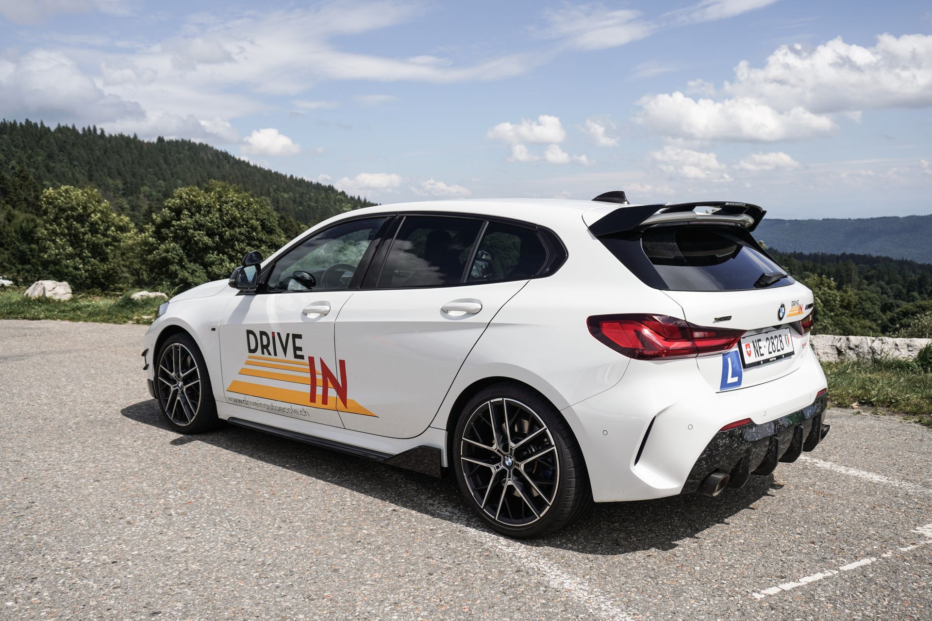 Voiture de rallye blanche à hayon sur une route de montagne avec des autocollants de sponsors et un aileron arrière