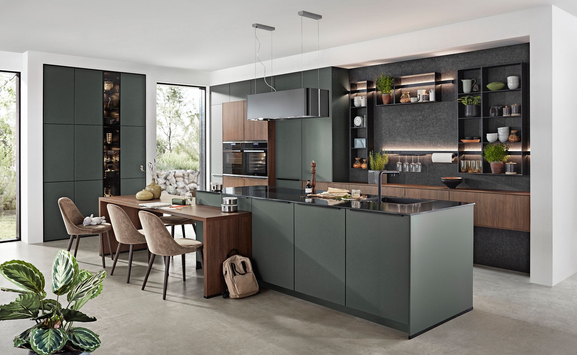 Cocina moderna con gabinetes verde oscuro, isla, mesa de comedor y estantes abiertos.