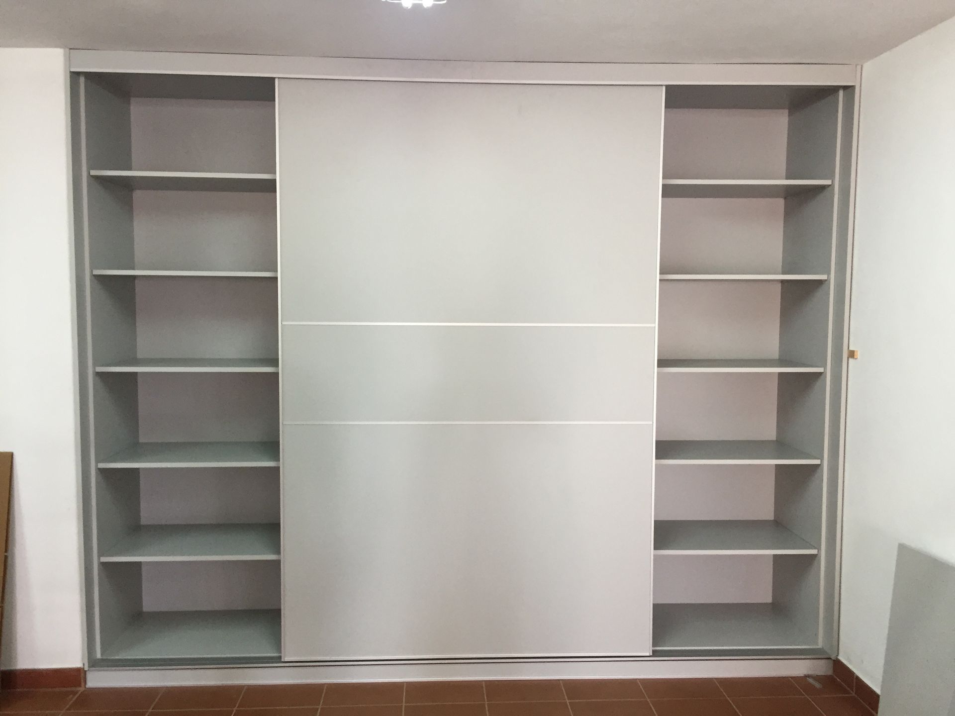 Un armario blanco con puertas correderas y estantes.