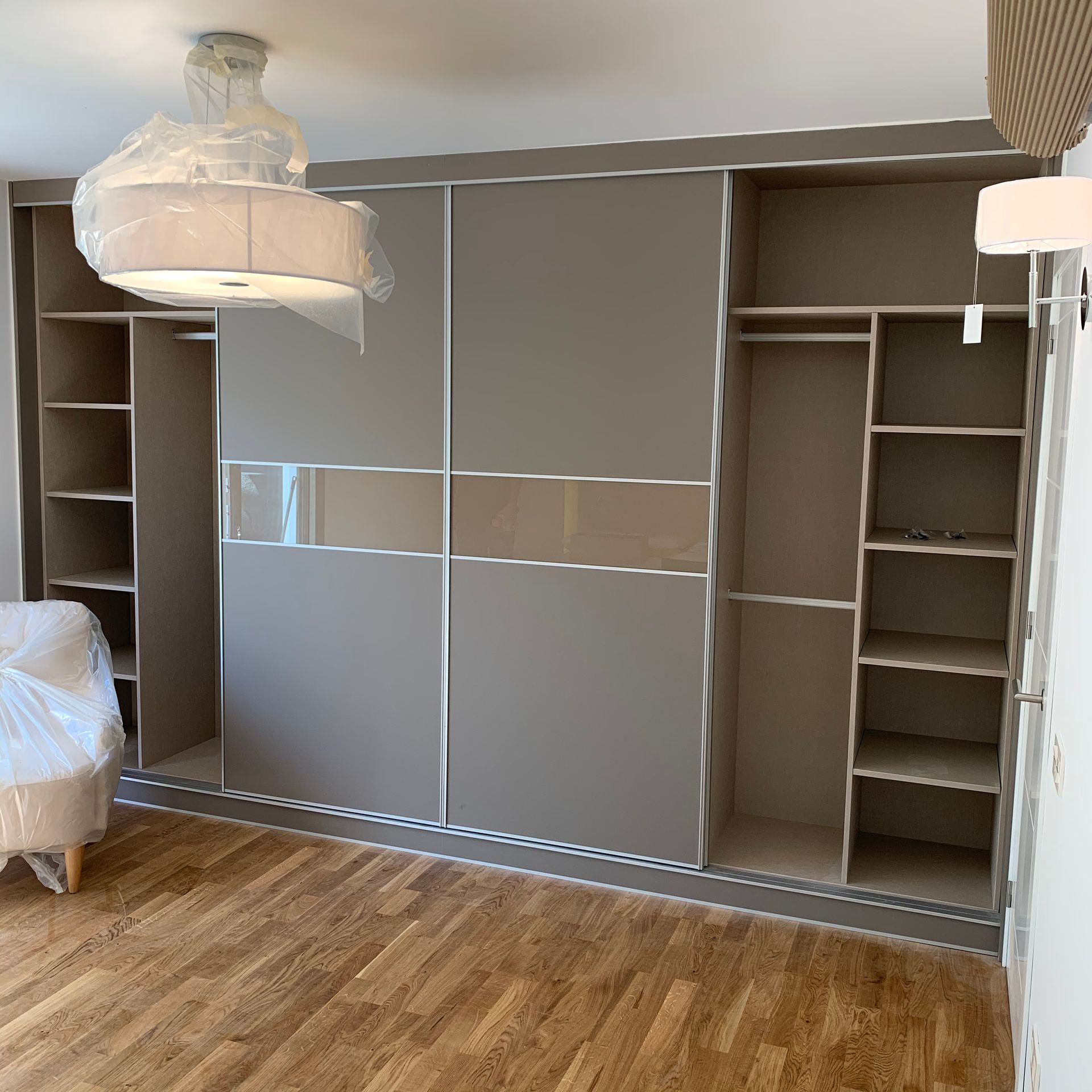 Un dormitorio con puertas corredizas de vidrio, estantes, una silla y una lámpara.