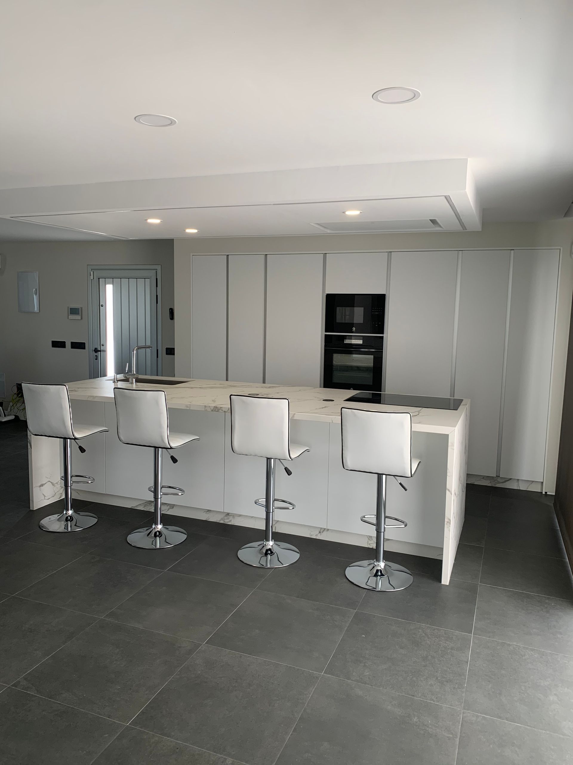 Una cocina con gabinetes y taburetes blancos y una isla grande.