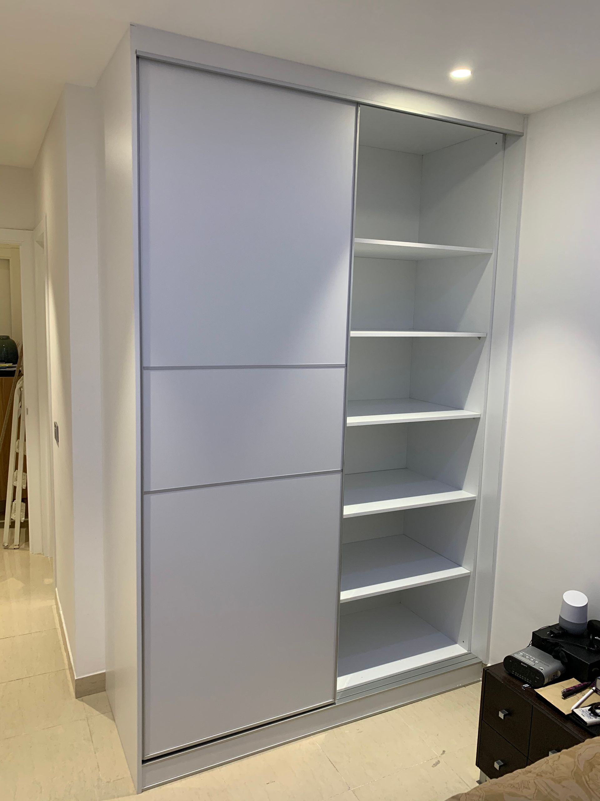 Un armario blanco con puertas correderas y estantes en una sala de estar.