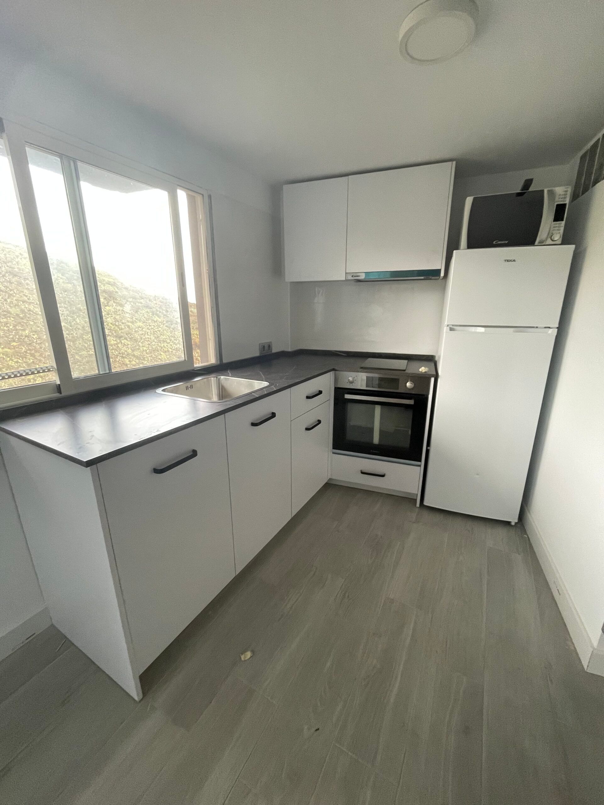 Una cocina con gabinetes blancos, un refrigerador, un horno y un fregadero.