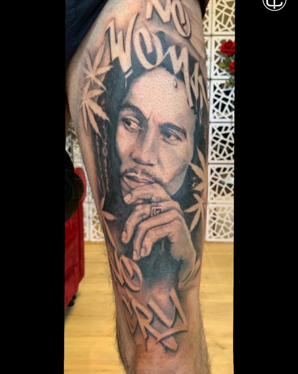 Un tatouage sur la jambe représentant un portrait de Bob Marley entouré de feuilles de cannabis et portant l'inscription « No Woman, No Cry ».