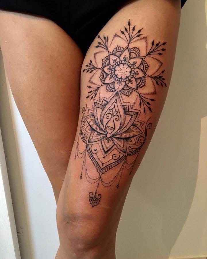 Un tatouage à l'encre noire sur une cuisse représentant un mandala symétrique superposé à une fleur de lotus détaillée.