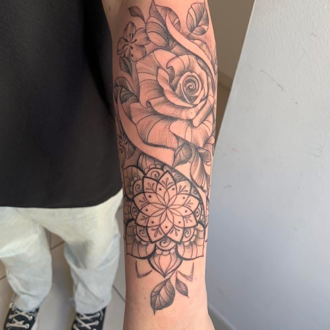 L'avant-bras d'une personne orné d'un tatouage détaillé à l'encre noire représentant une grande rose au-dessus d'un mandala complexe.