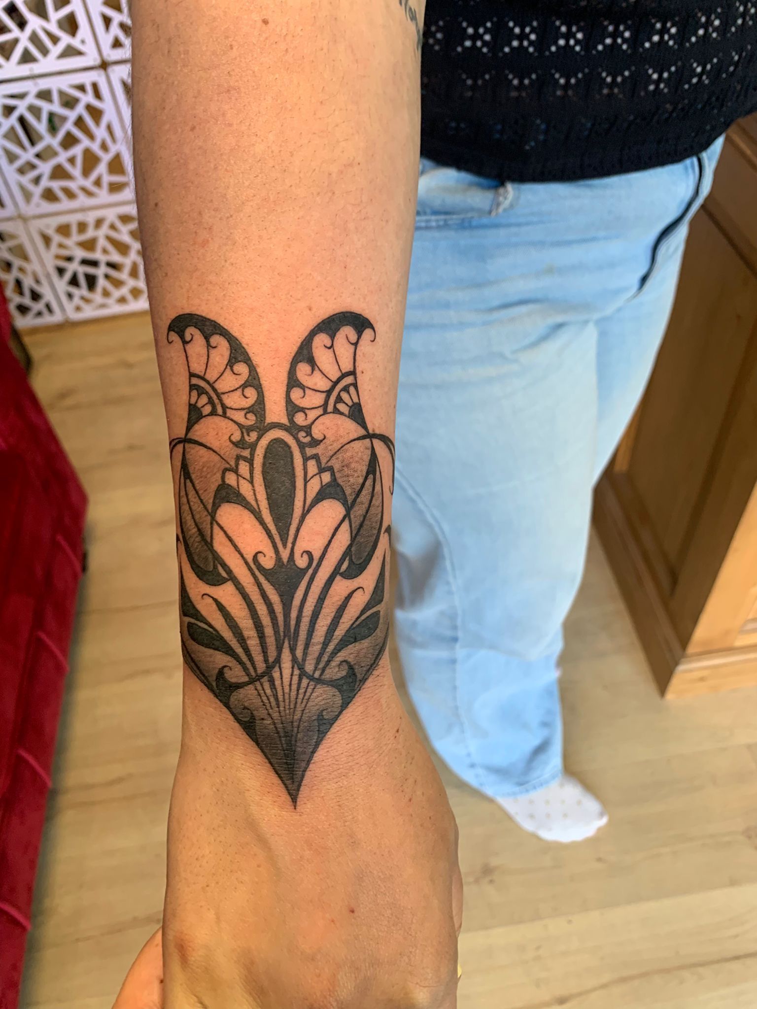 Un tatouage ornemental à l'encre noire présentant des motifs complexes et symétriques sur l'avant-bras d'une personne.