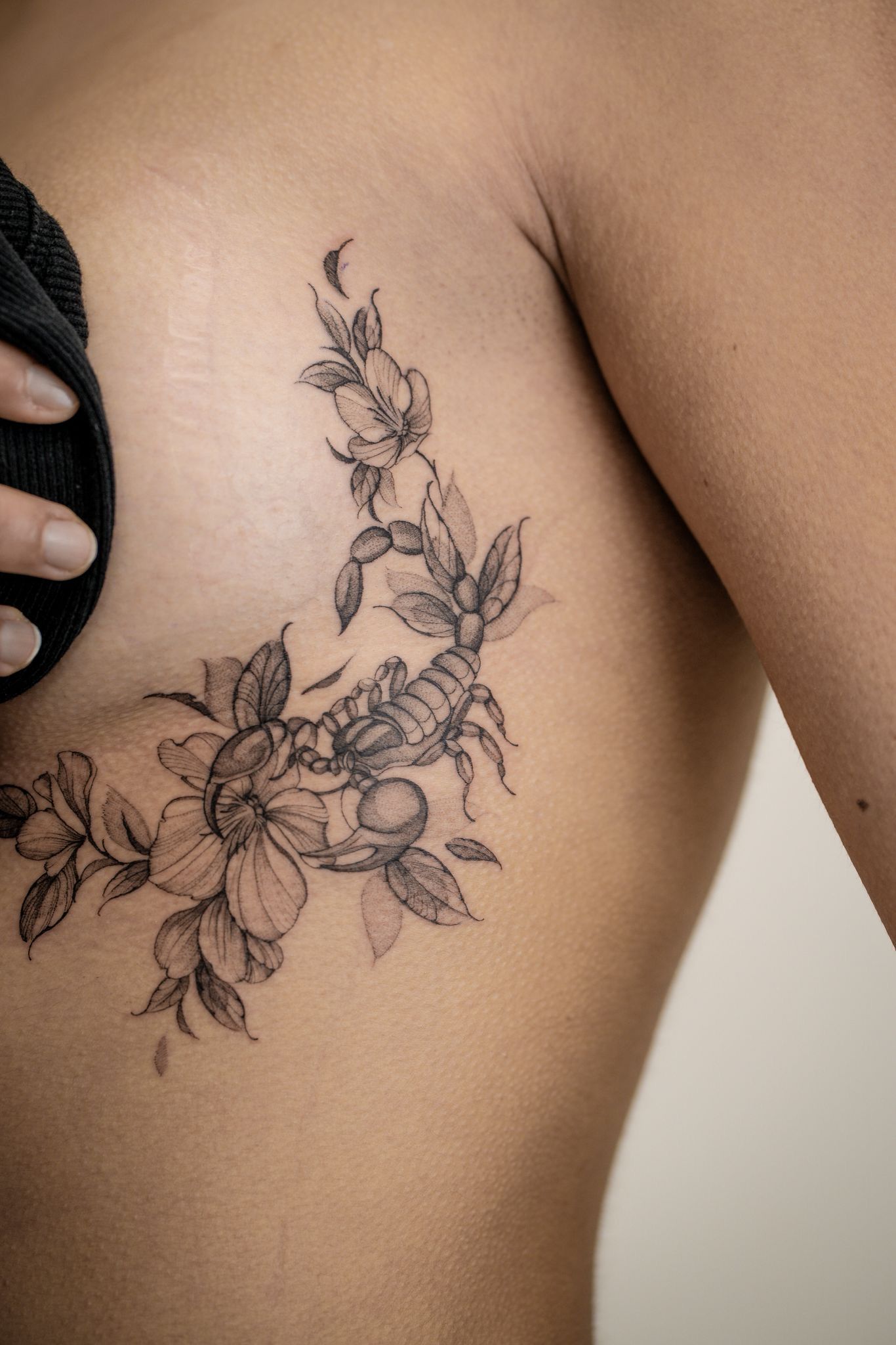 Un tatouage floral délicat représentant un scorpion, encré sur le côté du torse.