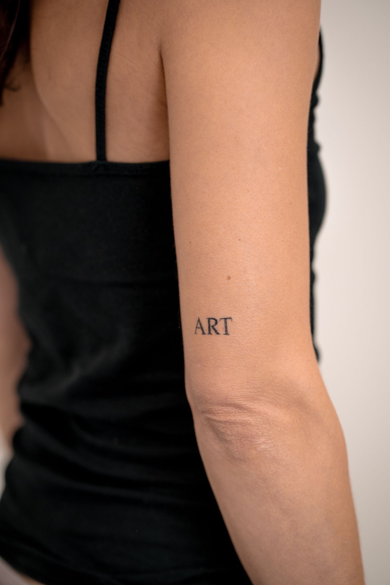 Gros plan sur un bras orné d'un petit tatouage noir à empattements où l'on peut lire « ART » sur la peau.