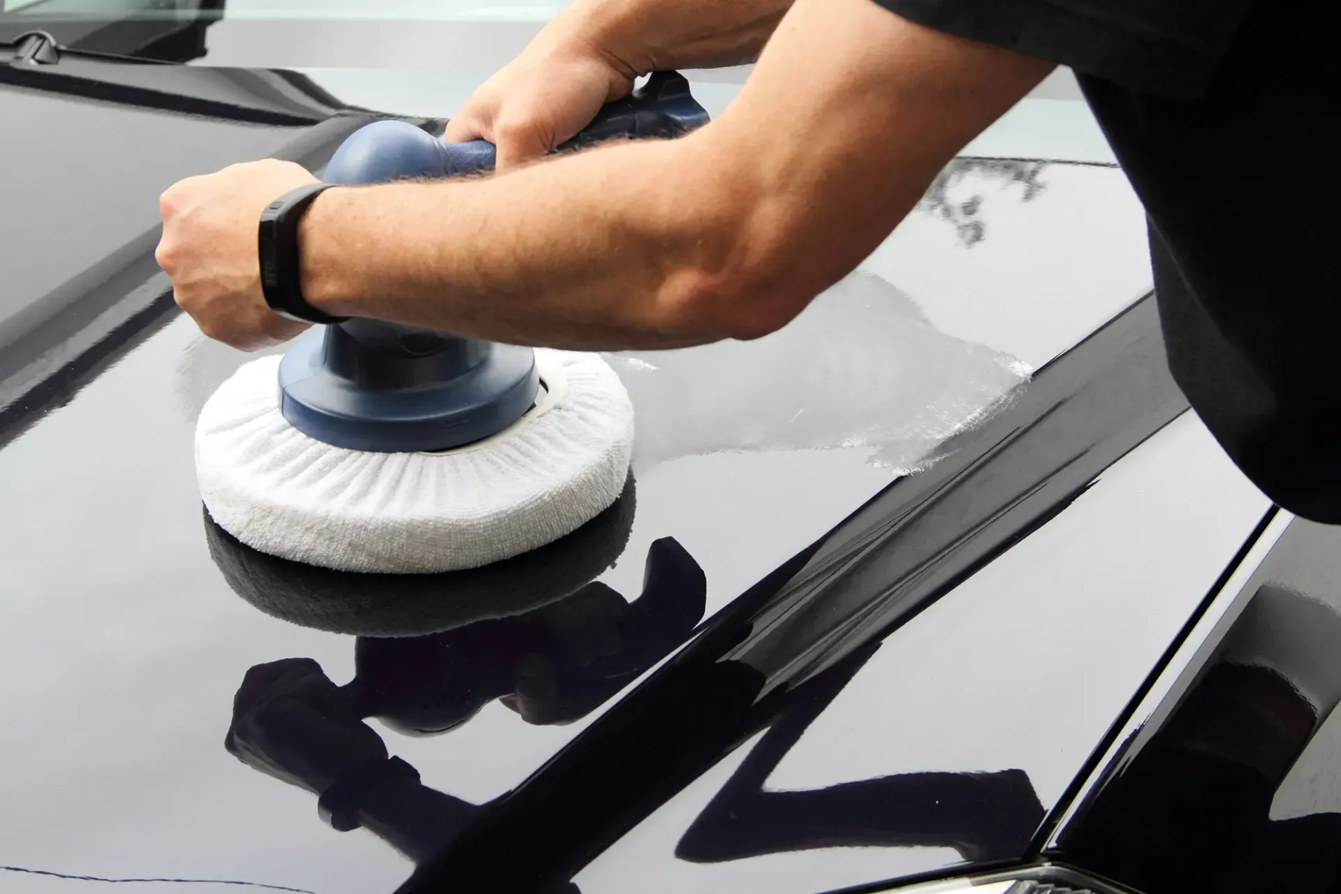 Ein Mann poliert die Motorhaube eines schwarzen Autos