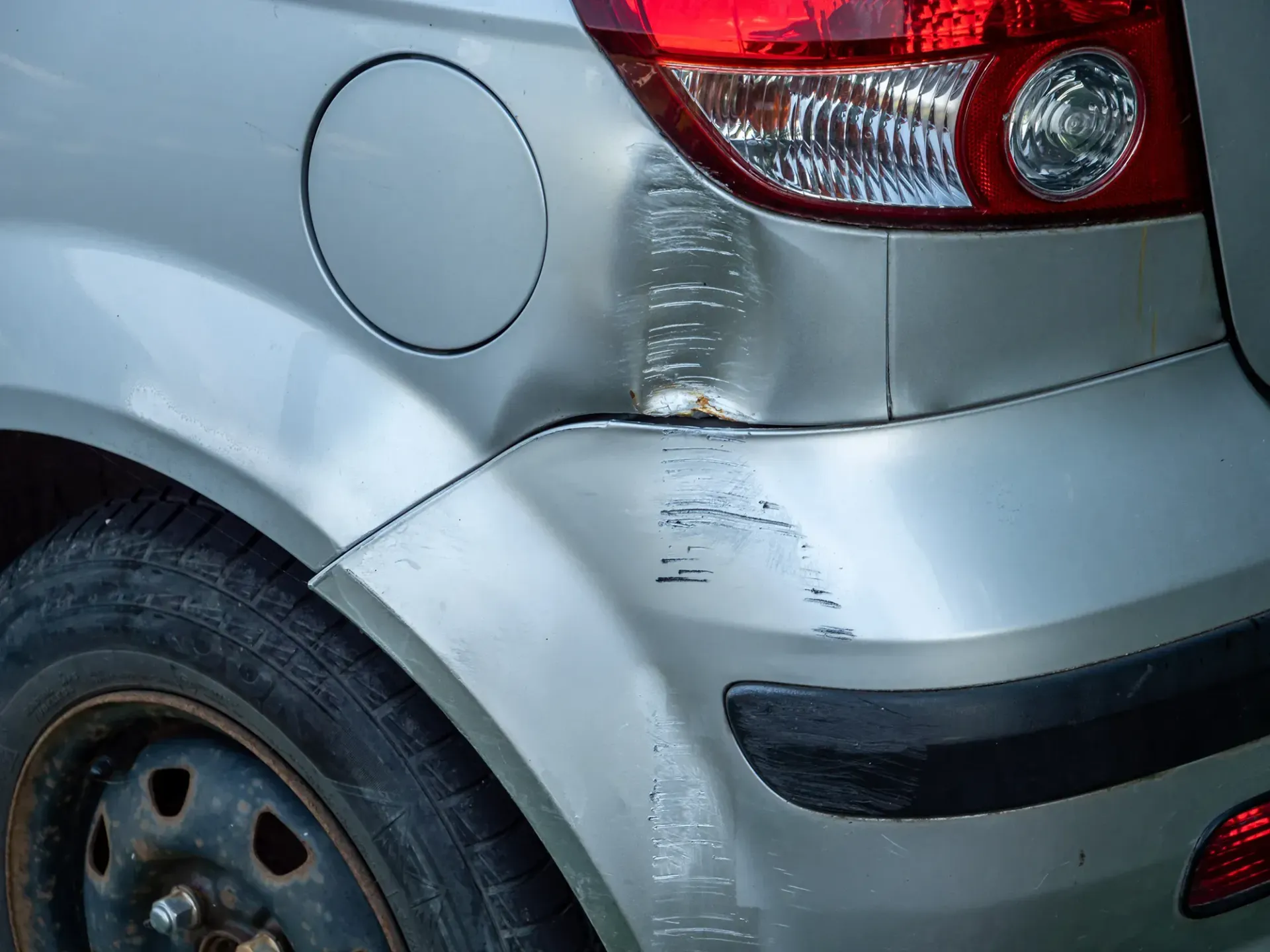 Ein silbernes Auto mit beschädigter Stoßstange steht am Straßenrand.