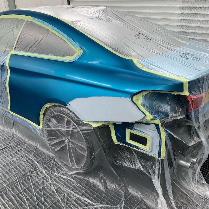 Ein blaues Auto wird mit Plastik überzogen und lackiert.