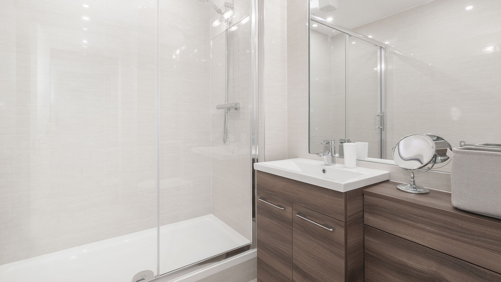 Baño moderno con ducha, lavabo, espejo y mueble con acabados en madera. Tonos blanco y marrón.