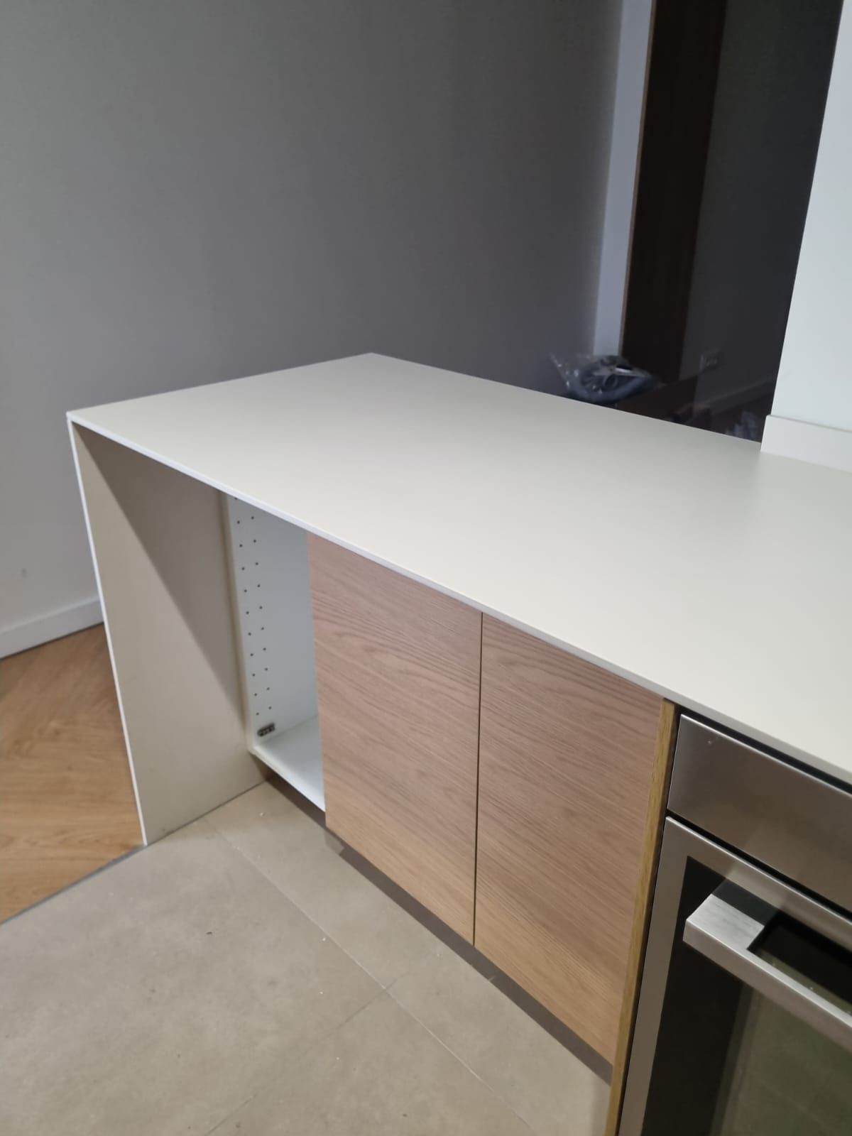 Encimera blanca con puertas de gabinete de madera clara y horno de acero inoxidable.