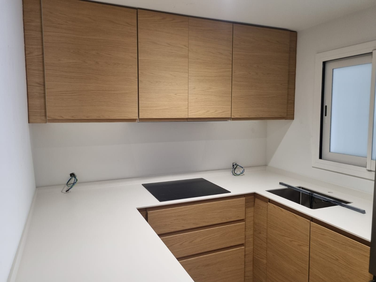 Gabinetes de cocina de roble con encimera blanca y estufa y fregadero integrados.