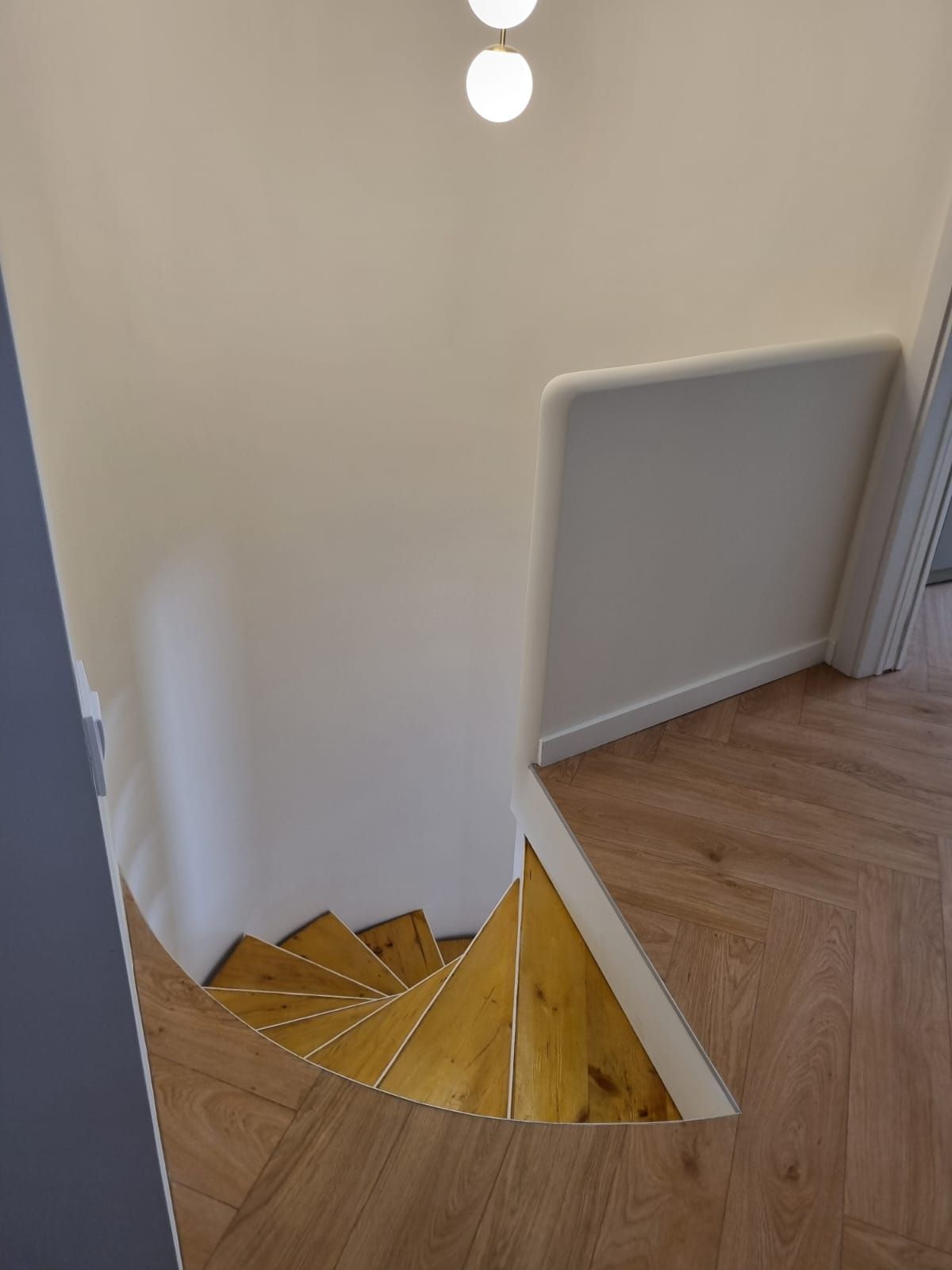 Escalera de caracol de madera con suelos de madera clara y paredes blancas.