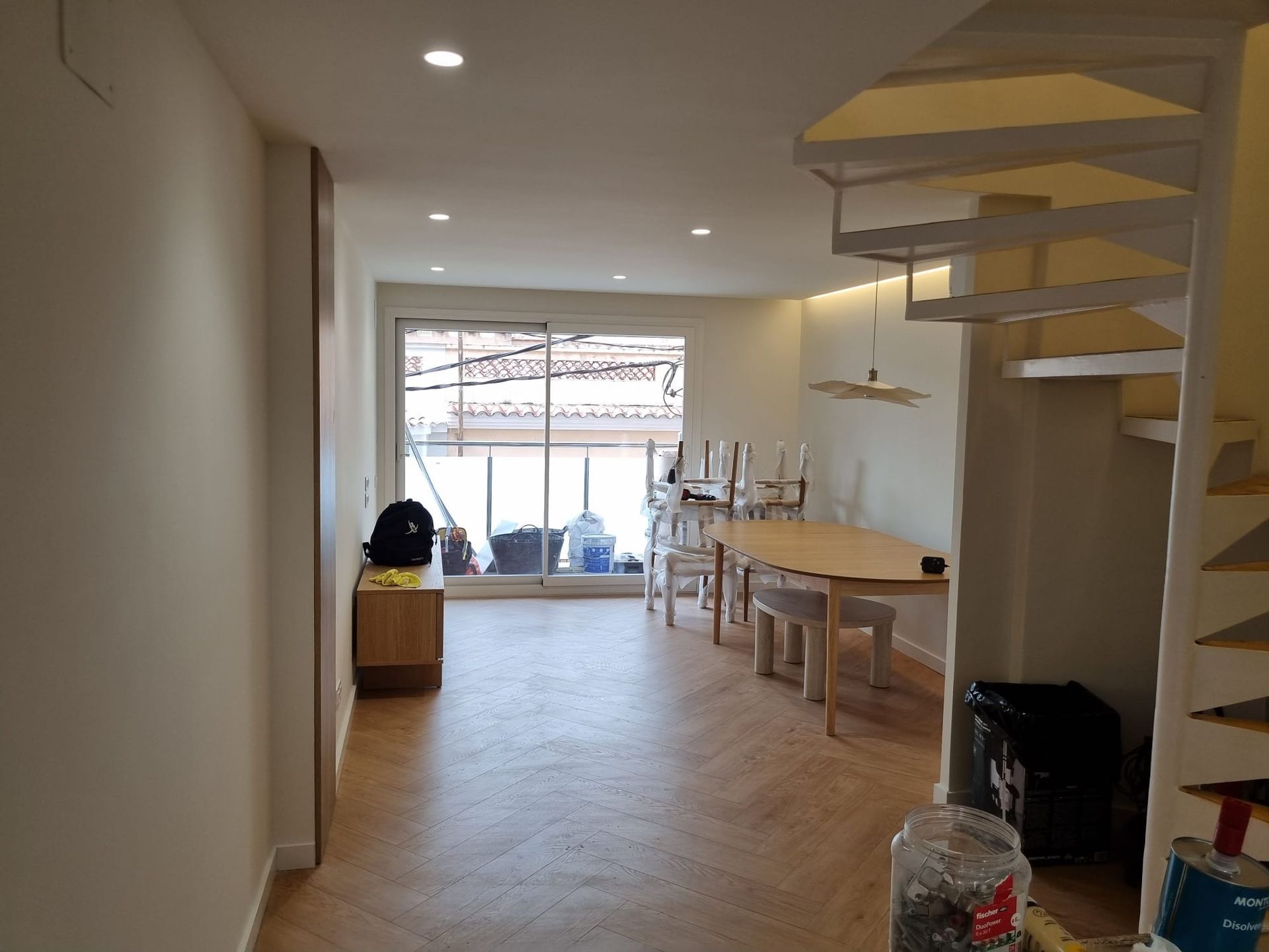 Fotografía interior de una casa con comedor, escalera de caracol y ventanal. Suelo de madera clara.
