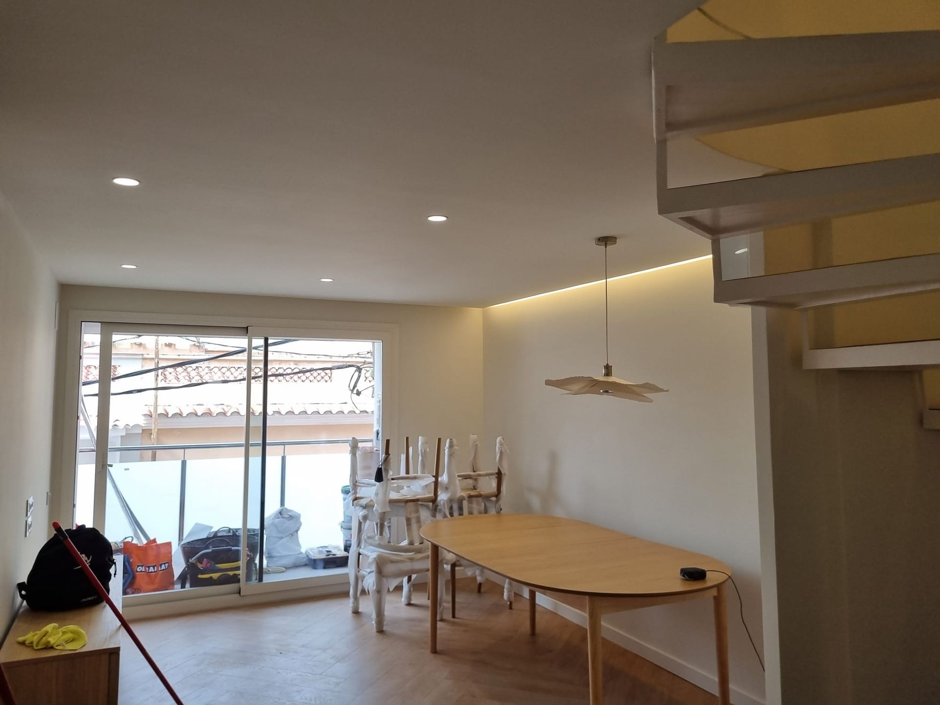 Comedor luminoso con mesa y sillas de madera clara, cerca de puertas corredizas de vidrio y escaleras.