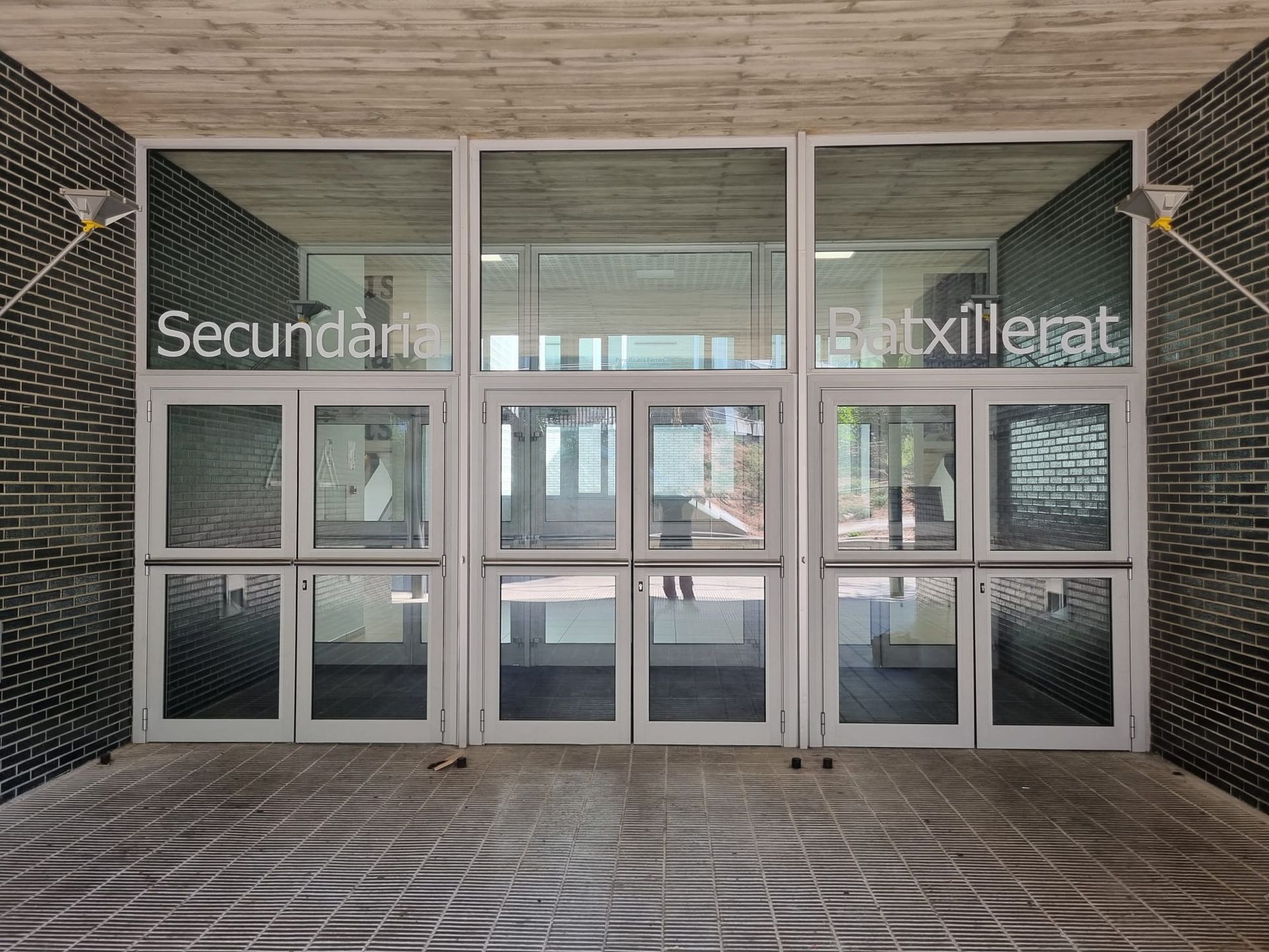 Puertas de entrada a Secundaria y Bachillerato. Puertas grises, paredes de ladrillo y suelo de baldosas.