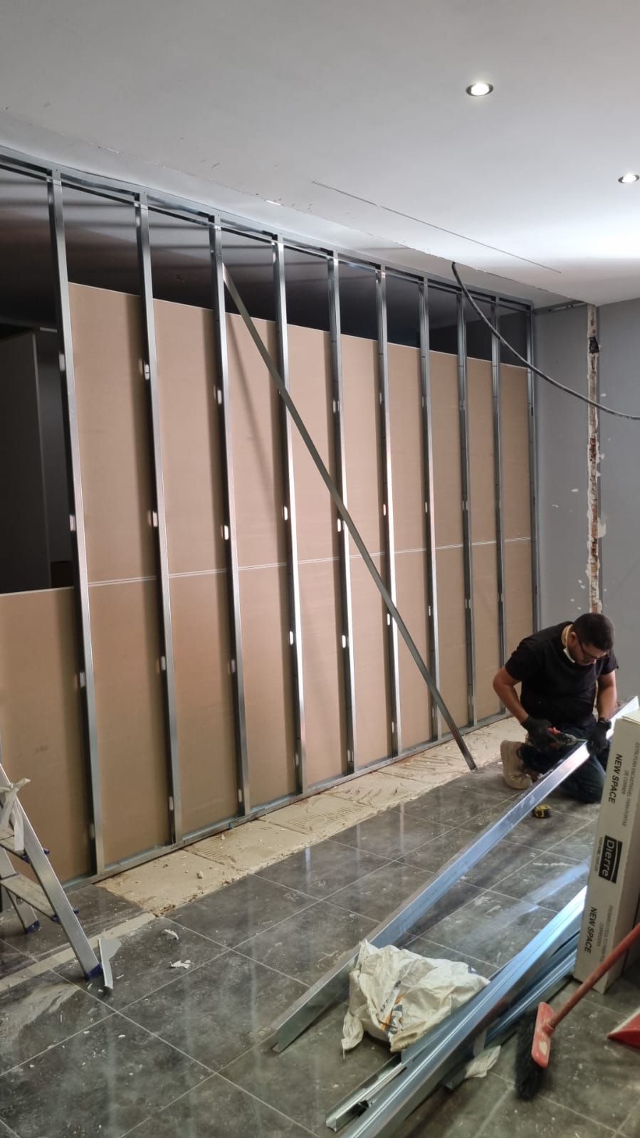 Hombre instalando paneles de yeso en una pared con estructura de metal en una habitación; construcción.