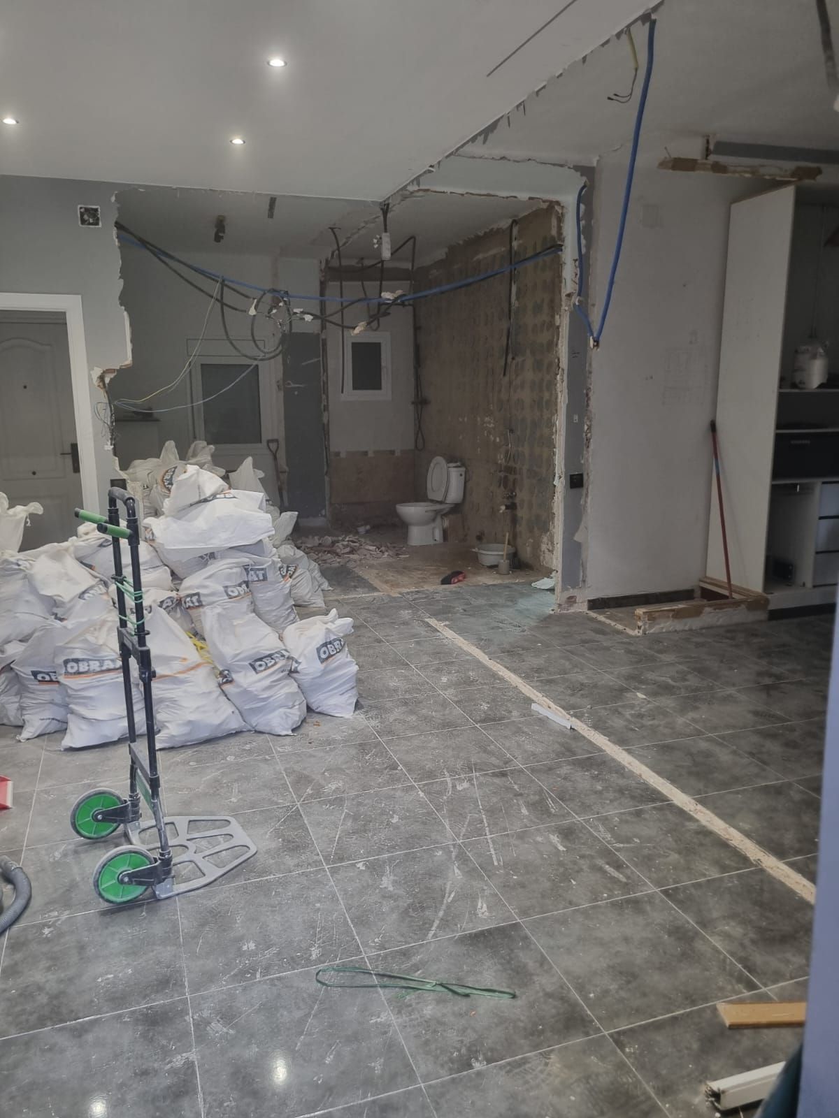 Renovación en progreso: habitación con bolsas de escombros, paredes expuestas, inodoro y una carretilla manual.