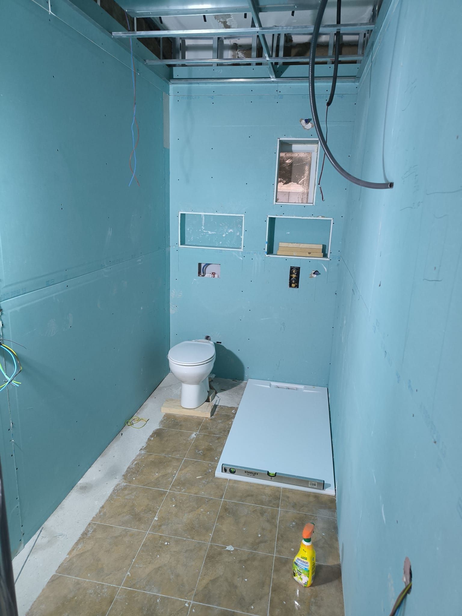 Interior de un baño en construcción; panel de yeso azul, inodoro, piso y un nivel.
