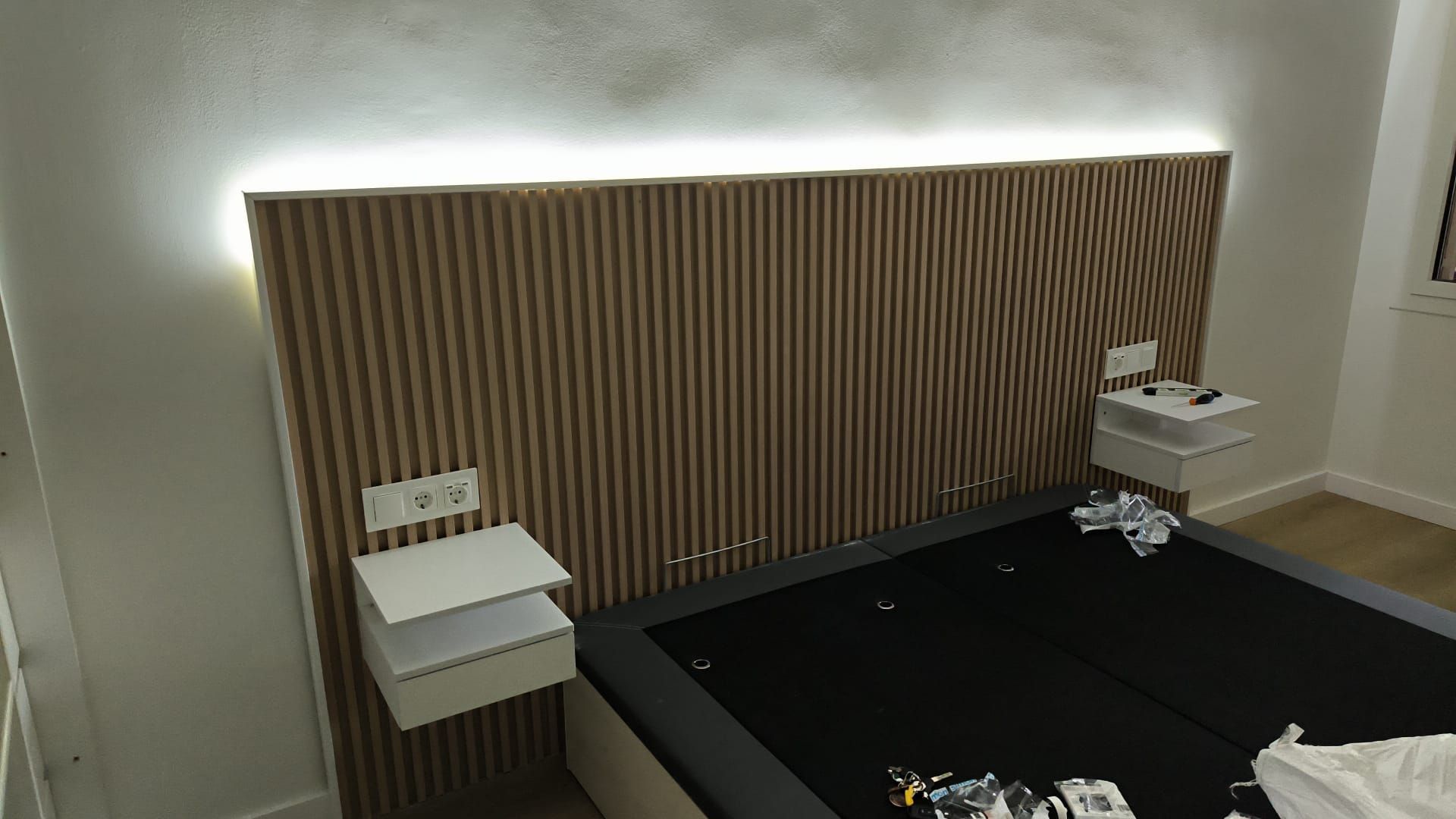 Dormitorio con cabecera revestida de madera, iluminación integrada, mesitas de noche flotantes